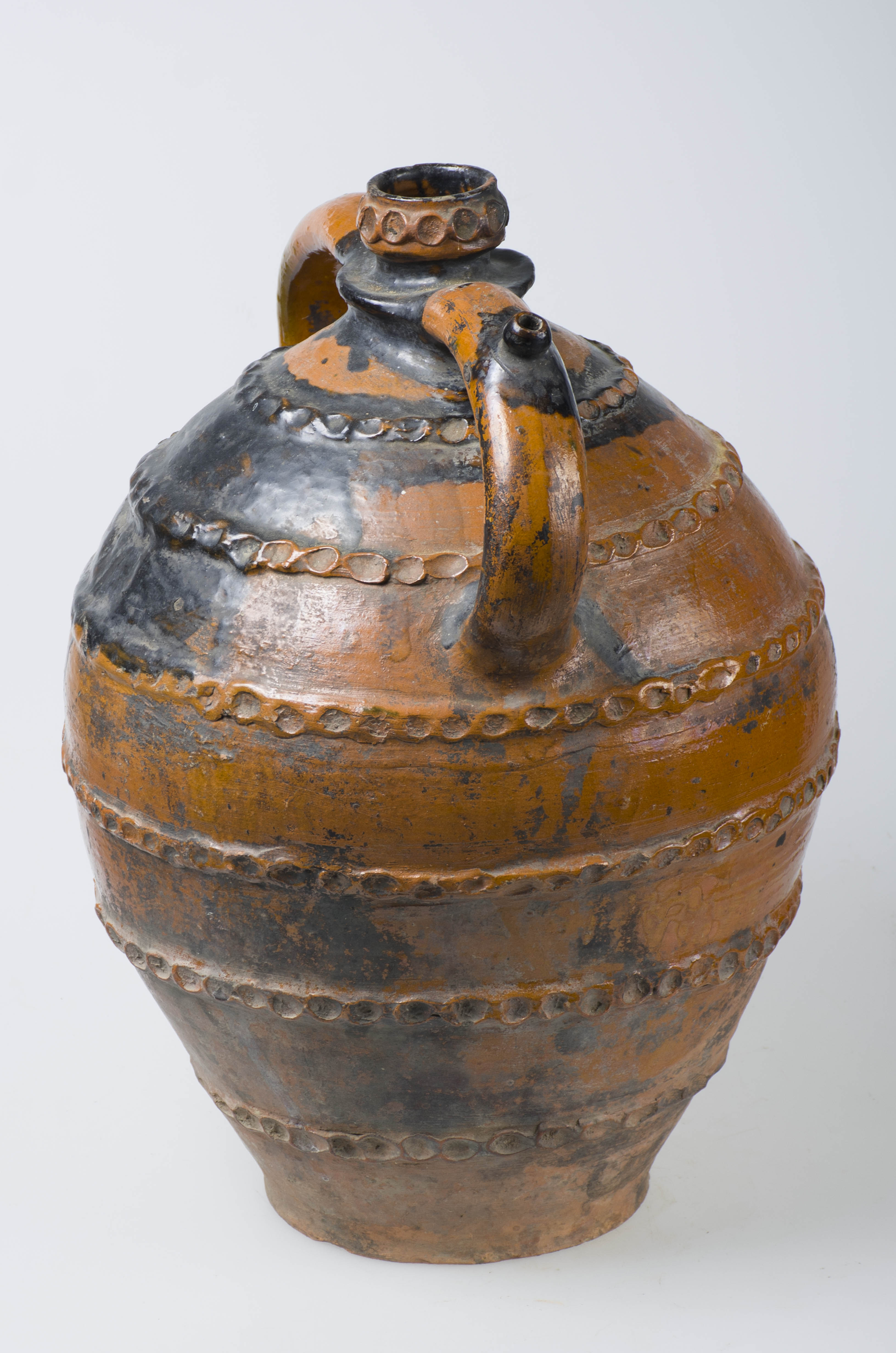 Vas ceramic de formă sferică cu gât îngust. Prezintă două toarte laterale din care una cu ”țâță”. Decorat în registre: șase brâuri alveolate și unul pe gât. Smălțuit pe toată suprafața superioară și mijlocie. Cromatică: crem; stropit cu maro pe partea superioară.