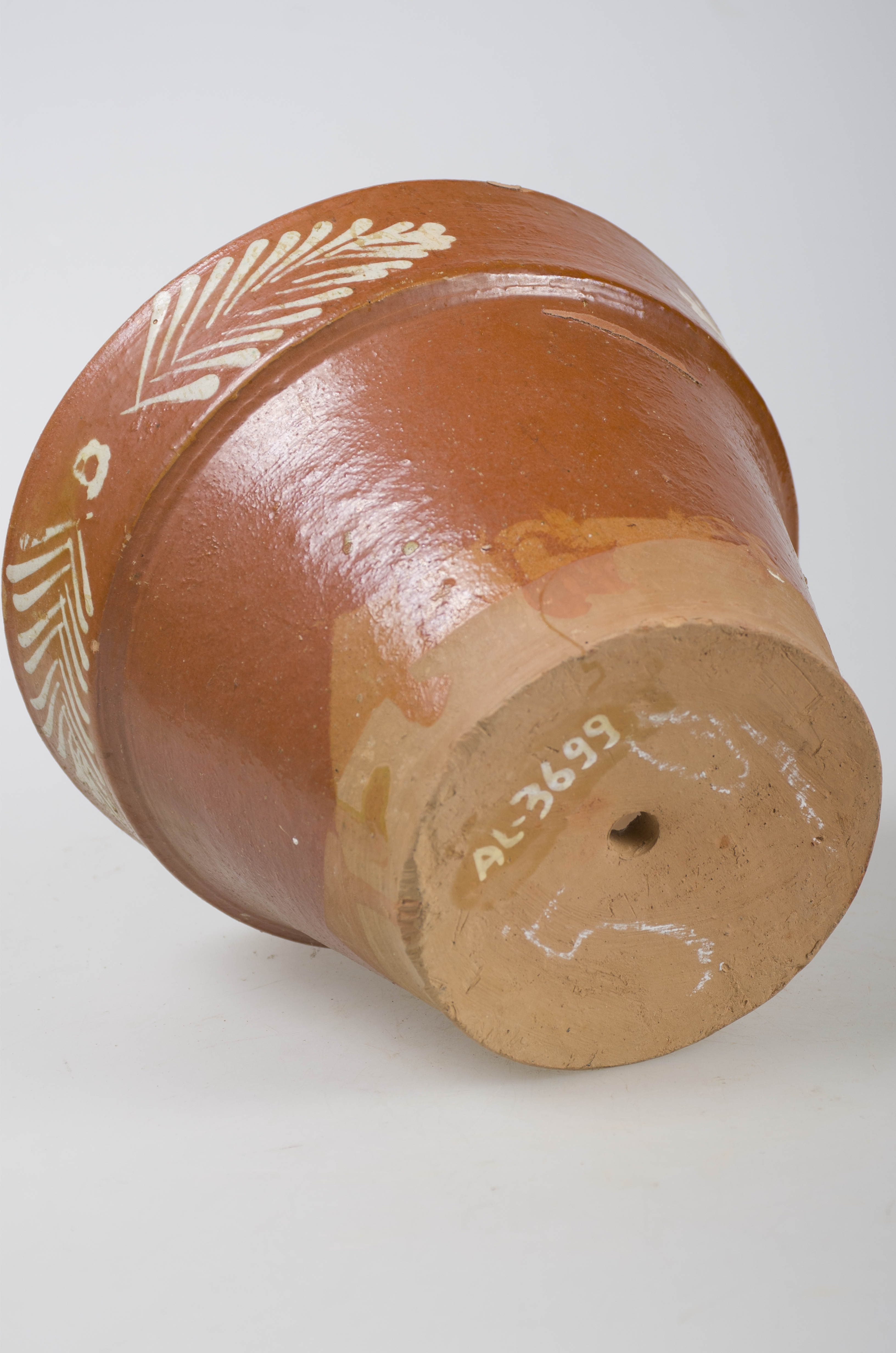Vas ceramic de formă tronconică cu baza plată și pereții înalți. Smălțit în exterior. Decorat în zona gurii cu motive fitomorfe: două perechi de frunze. Pe fund prezintă un orificiu pentru scurgerea apei. Cromatică: fond: maron-cărămiziu; motive: alb.