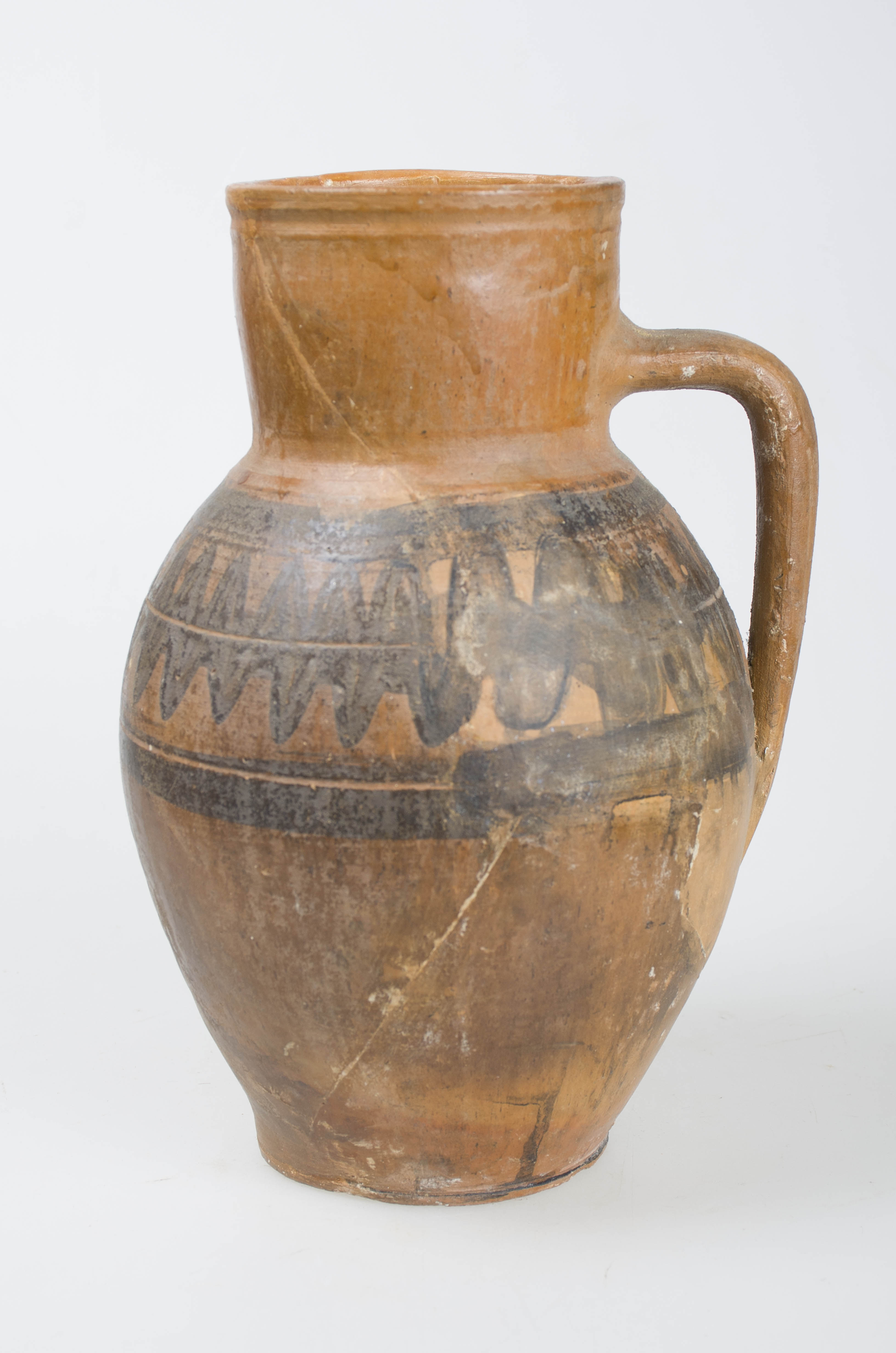 Piesă din ceramică, lucrată manual la roată. Piesa are corp sferoidal, bombată în partea mediană, cu gât cilindric. Între gât și mijlocul zonei bombate este așezată o toartă laterală. Imediat sub gură prezintă o linie circulară incizată. Piesa prezintă decor realizat cu ajutorul formelor geometrice, două rânduri circulare de linii ondulate încadrate între două linii circulare paralele. Cromatică: cărămiziu; negru.
