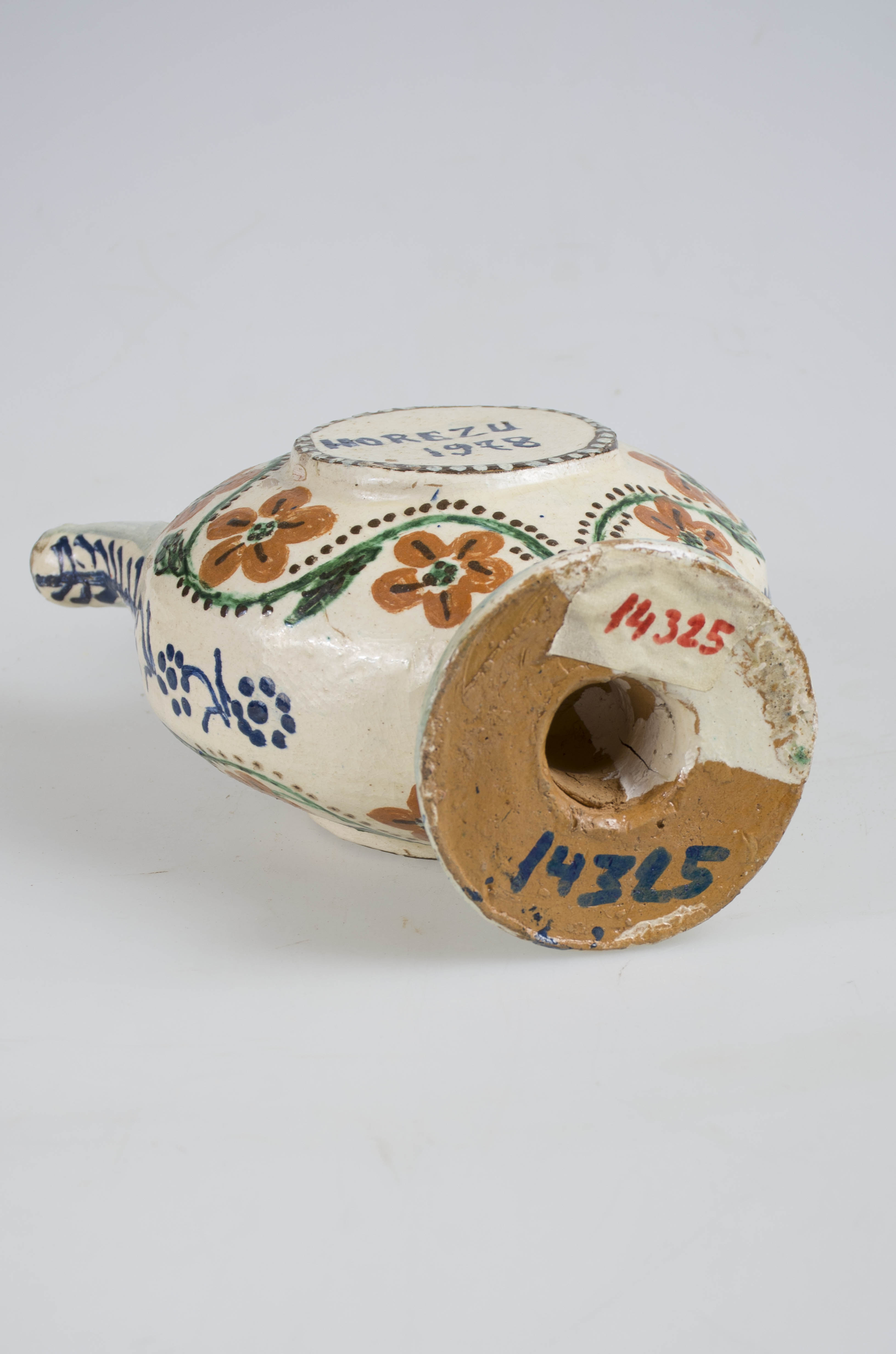 Vas ceramic de formă sferoidală aplatizată, susținut pe o bază inelară, cu câte o parte rotundă pe cele două fețe ușor evidențiată în exterior și conturată cu o linie maron închis cu puncte albe, având inscripția ”HOREZU 1978” pe ambele părți. Gât scurt îngust cu gură circulară, prezintă toartă și picurător acestea din urmă fiind dispuse pe cant. Toarta, gura și picurătorul decorate linii albastre. Bilateral inscripțiile sunt încadrate de către o linie verde puternic ondulată dublată de două linii punctiforme negre de-a lungul fiind dispuse șapte flori cu petale cărămizii și frunze verzi. Cromatica: fond: alb; motive: verde; negru; albastru; cărămiziu; maro închis.