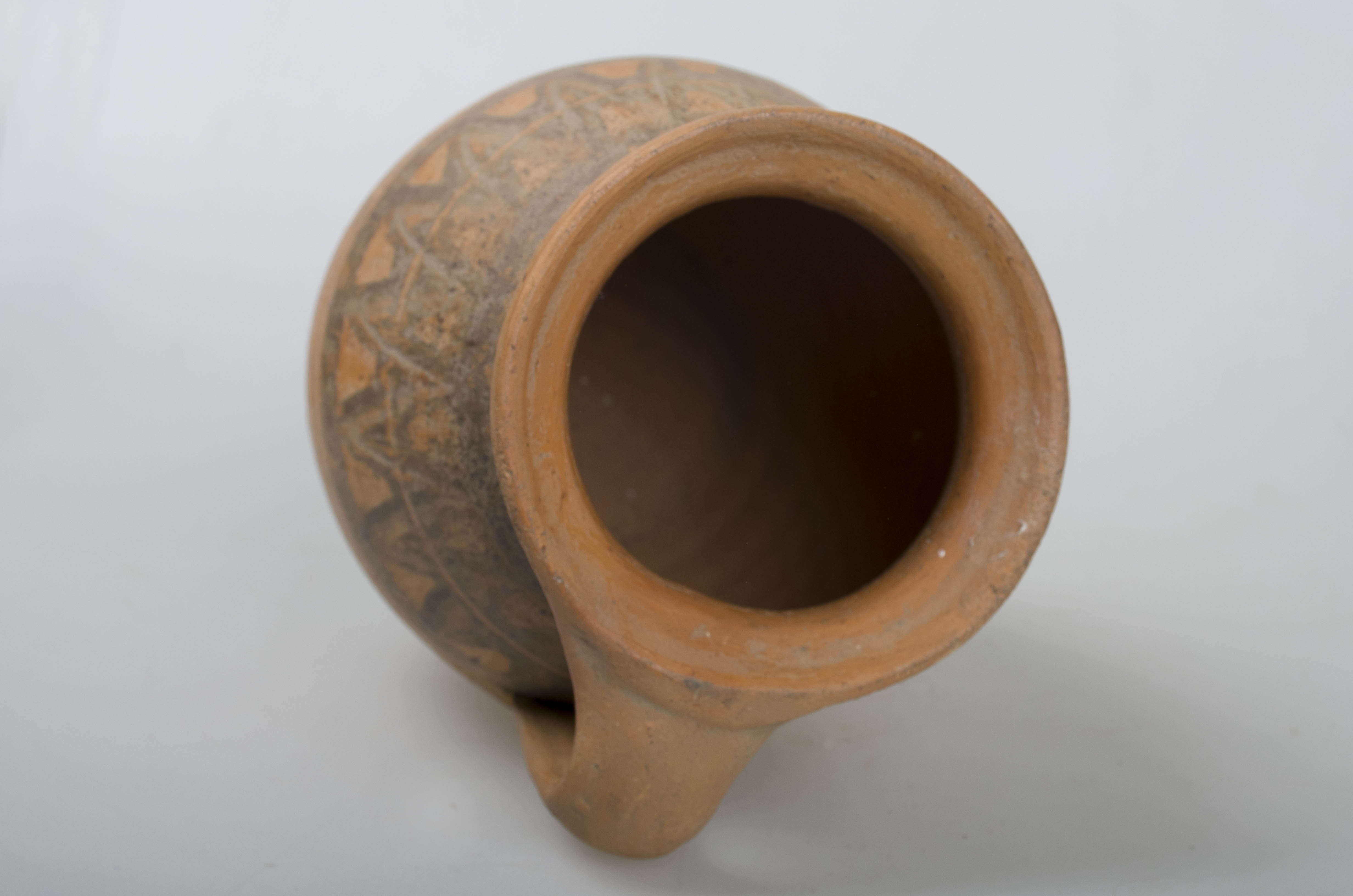 Vas ceramic de formă ovoidală cu gât larg și scurt, marginea gurii evazată și buză dreaptă. Prezintă o toartă ce leagă gura vasului cu partea de diamentru maxim. Ornamentații în partea superioară a ulciorului ilustrând motivul dintelui de lup, specific centrului ceramic Săcel, dispus în alternanță pe ambele părți a unei linii continue incizate dispuse circular, încadrată de două dungi negre. Peste registrul decorativ principal se suprapun ușoare incizii ce urmează linia decorației centrale. Cromatică: cărămiziu; negru.