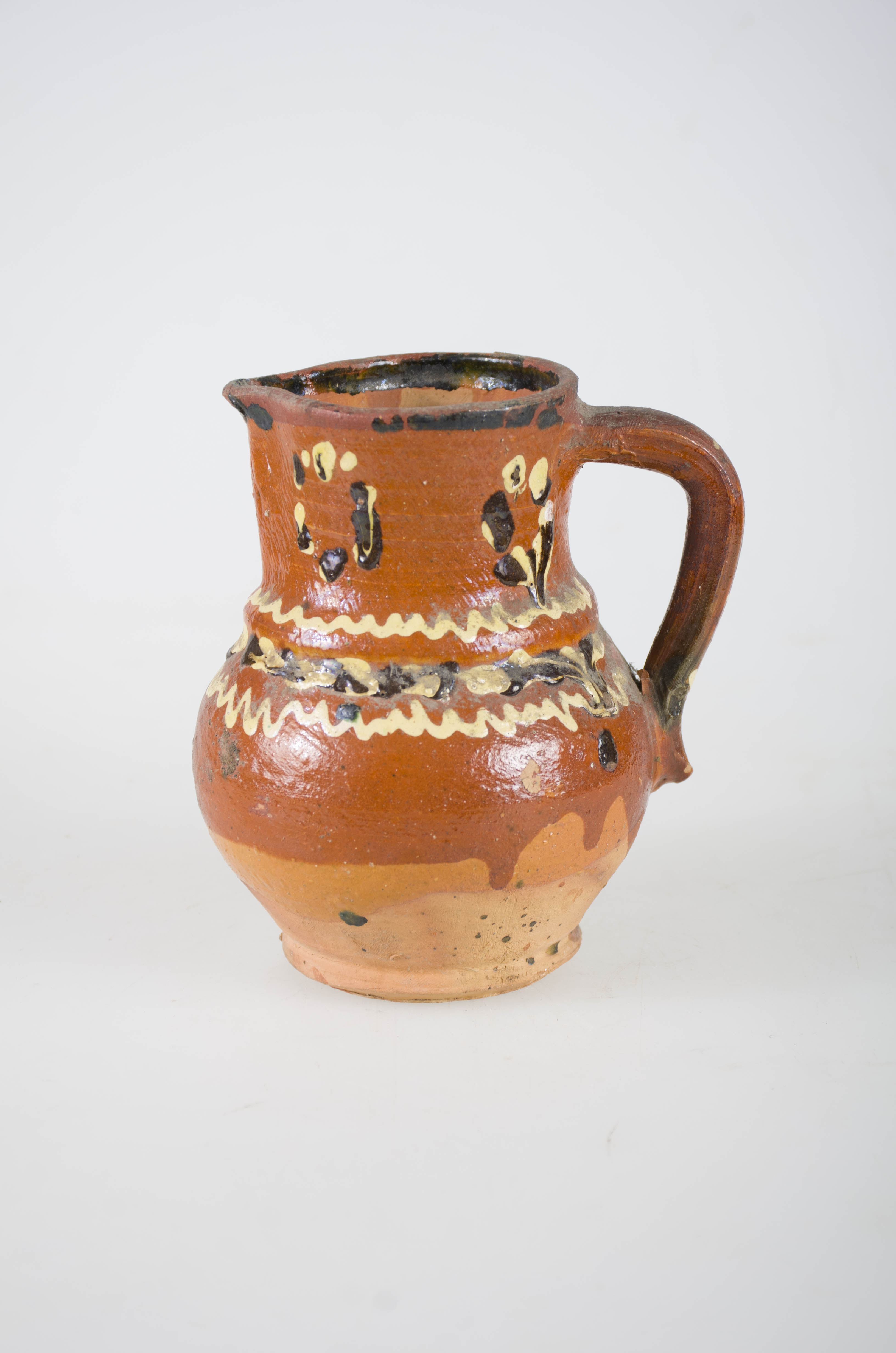 Obiectul este realizat din material ceramic, având forma tronconică și buza ușor evazată. Din partea superioară până în zona mediană a vasului pornește o toartă realizată din același material destinată prinderii sau agățării obiectului. Tot în partea superioară prezintă un canal destinat curgerii lichidelor din interior. Cana este smalțuită. Din punct de vedere al ornamentației se remarcă motive geometrice și vegetale realizate cu alb și negru pe fond caramiziu. Fundul obiectului este plat.