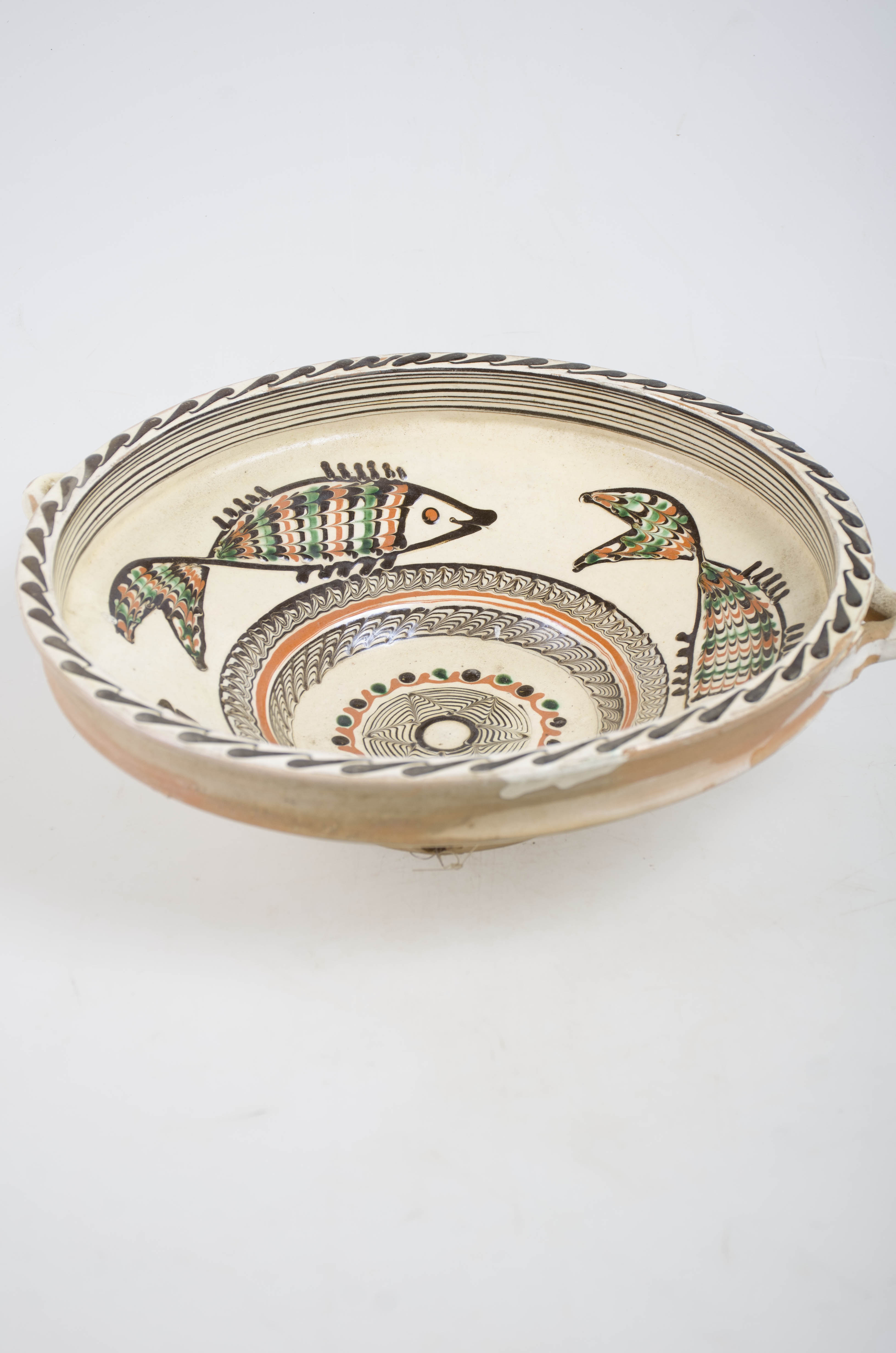 Vas ceramic de formă tronconică, ce prezintă baza adâncită din care pornesc pereții arcuiți spre exterior terminându-se cu margine dreaptă și buza plată. Ornamentica realizată cu cornul este pe fond de angobă dispus pe două registre. Pe fundul vasului avem o stea în sașe colțuri încadrată de un "șir cu puncte" locul de ornamentație între buză și pereți "jirăvit". Pereții ornamentați cu trei pești, marginea cu cercuri concentrice, iar pe buza dreaptă o linie ondulată. Pe fundul vasului apare numele meșterului și localitatea "Ogrezeanu Stelian - Horezu". Cromatică: maro, verde, alb, maro roșcat. Smălțuit în interior.