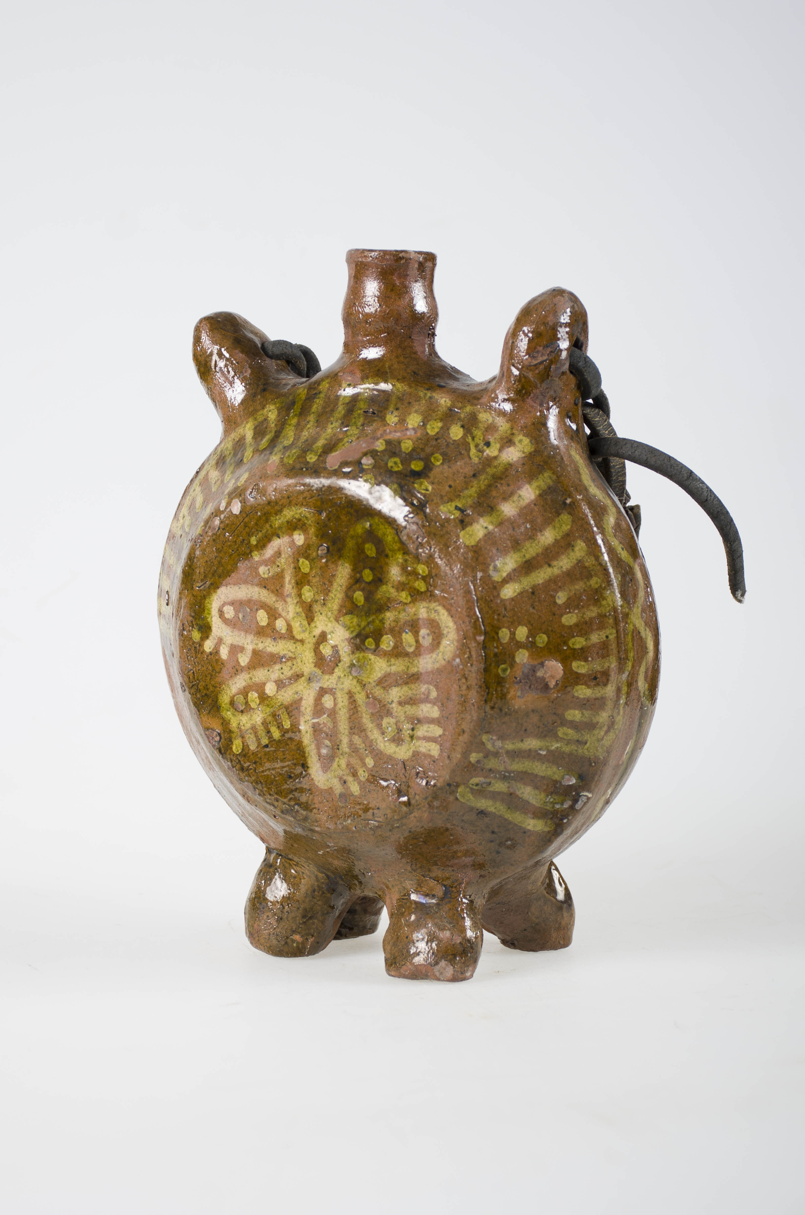 Piesă formată din corpul ceramic de formă circulară, cu gura înaltă și foarte îngustă și curelușa de piele. Este smălțuită în interior și exterior. În partea superioară a corpului prezintă două urechi (de care se leaga curelușa). În partea inferioară prezintă patru piciorușe scurte pe care se sprijină. Este decorată pe ambele fețe cu motive florale: câte o floare cu șapte petale umplute cu câte trei puncte și mărginite de linii scurte paralele. Motivul floral central este încadrat de motive geometrice: linii dispuse în formă de raze de soare întrerupte din loc în loc de câte o floare stilizată realizată din puncte. Cantul obiectului este ornamentat cu o linie în zona dintre urechi și piciorușe. Cromatica: fond: maro; motive: alb-verde.
