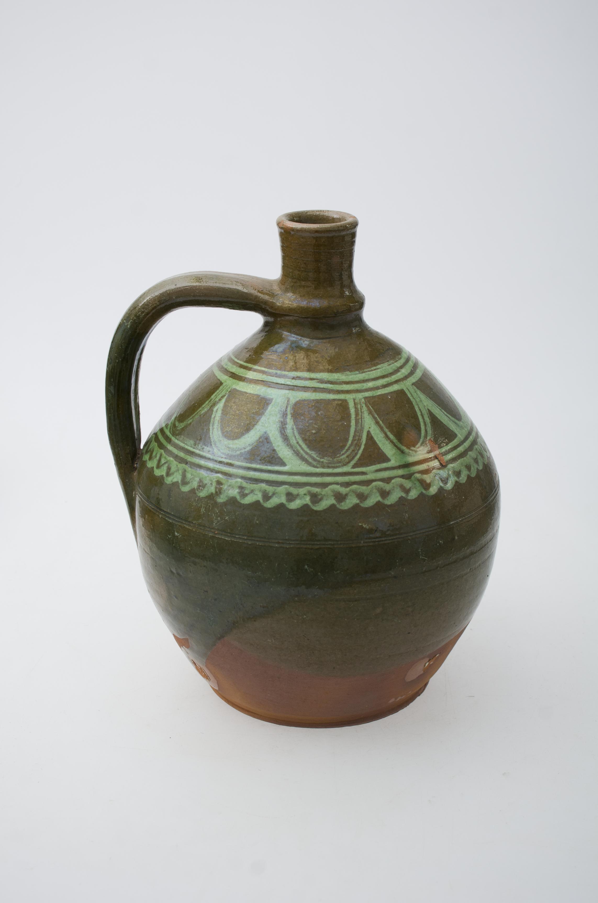 Recipient ceramic bitronconic, cu baza dreaptă, gâtul înalt și ușor lărgit spre buză. Ulciorul prezintă o toartă, care pornește din zona gâtului și se unește cu corpul vasului, în zona diametrului maxim al acestuia. Umerii recipientului ceramic au fost decorați cu un registru pictural, compus din motive geometrizante: un val cu bucle ample, cuprins între linii paralele drepte și în valuri. În partea inferioră, în proximitatea fundului, vasul prezintă cromatică maro, nefiind pictat și smălțuit. Prezintă uzură funcțională. Cromatică: fond: maro, maro-verzui; motive: verde.