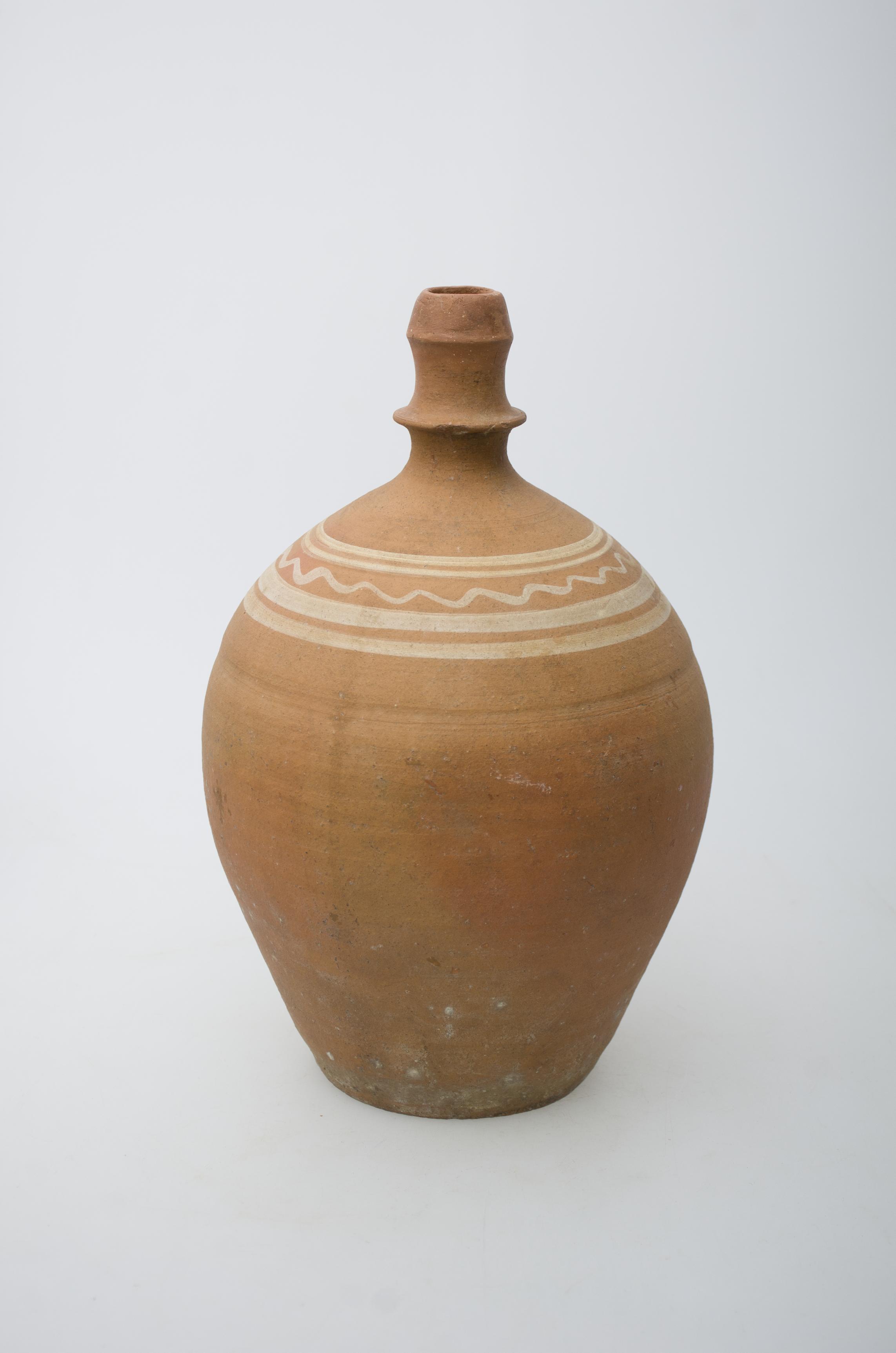 Recipient ceramic bitronconic, cu baza dreaptă, gâtul înalt și ușor restrâns spre buză. Ulciorul prezintă o toartă, care pornește din zona gâtului și se unește cu corpul vasului, în zona diametrului maxim al acestuia. Umerii recipientului ceramic au fost decorați cu un registru pictural, compus din motive geometrice: patru linii concentrice groase, dispuse paralel, și despărțite de o a cincea linie concentrică, în valuri. Cromatică: fond: cărămiziu; motive: alb.