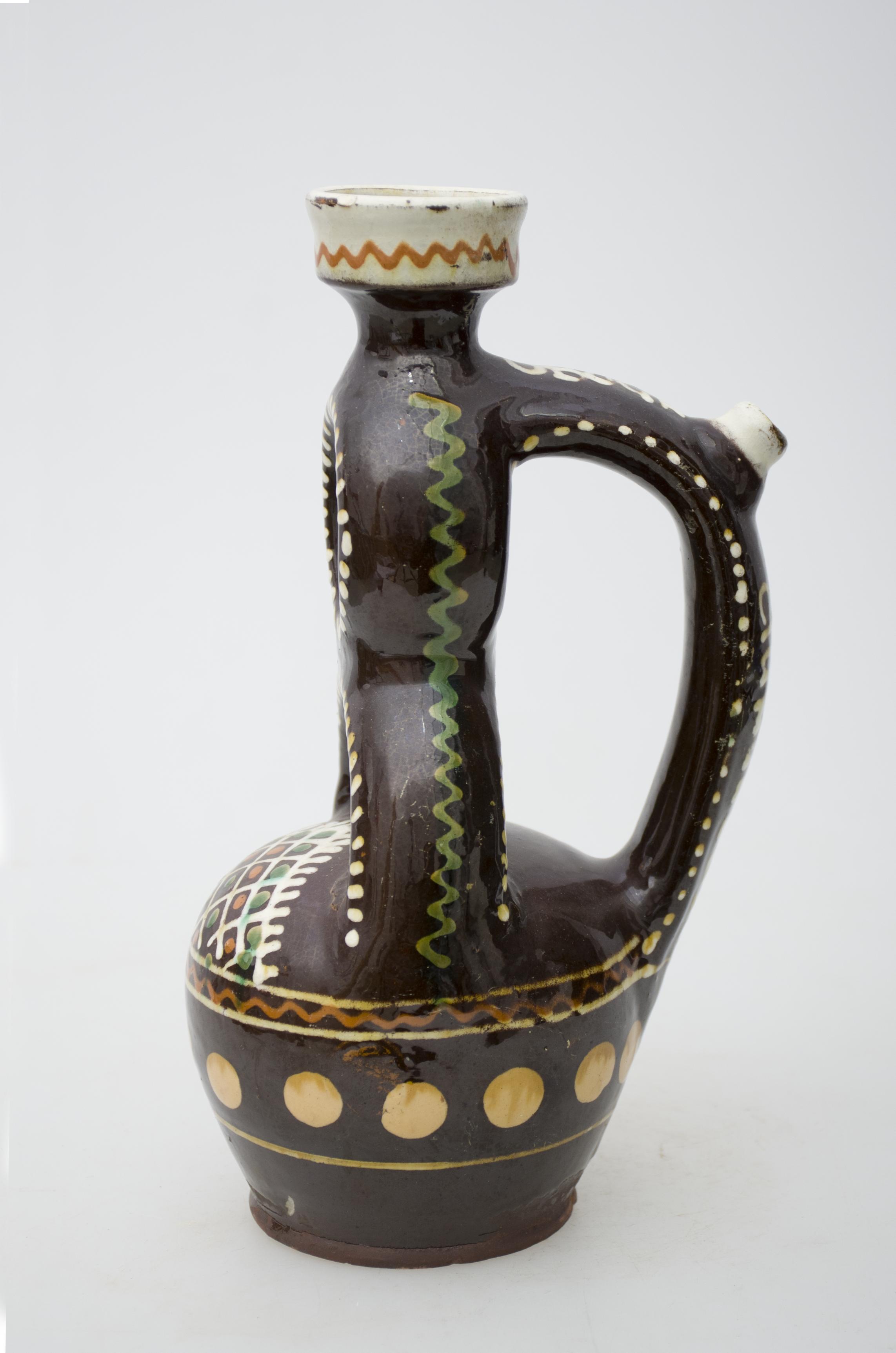 Recipient ceramic de formă sferică, având o prelungire tubulară de formă circulară suprapusă peste un semicerc, care se termină cu o gură cu manșon și gât scurt. Este smălțuit atât la interior cât și la exterior. Pe cant este prevăzută o ”țâță” pentru scurgerea lichidului. Tot aici este pictat centrul de olărit Oboga și numele meșterului olar, Grigoriu Ciungulescu. Intens stilizată cu motive geometrice și florale, pictate cu cornul; în zona gurii: linie meandrică albă; în zona tubulară: șiruri de puncte albe și o linie meandrică portocalie; în zona sferică: cercuri încadrate în romburi, alcătuind un triunghi cu laturile albe, pe două din ele fiind pictați franjuri și două flori cu petale subțirii; în partea inferioară: o linie meandrică de culoare maro încadrată între două linii circulare albe, un șir de buline crem. Aproape de fundul vasului, mai este pictată o linie fină, circulară. Cromatică: fundal maro închis; motive: alb, portocaliu, crem, maro, verde.