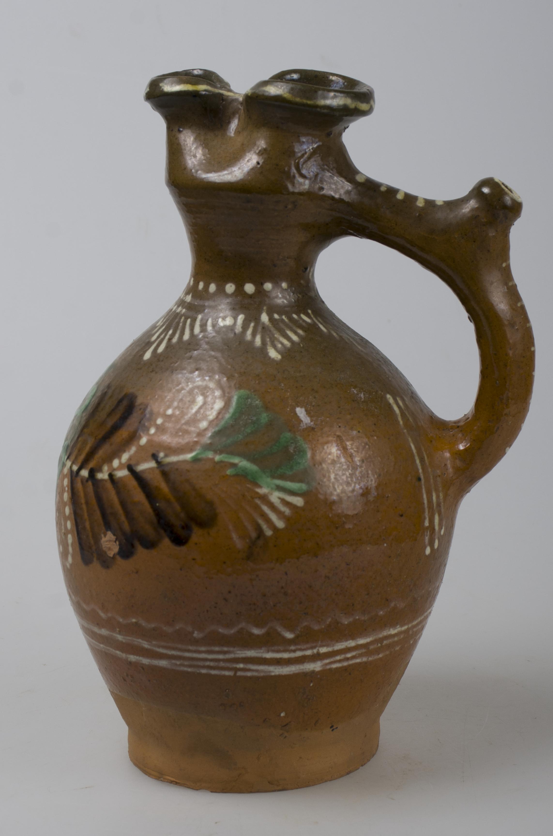 Vas ceramic bitronconic cu gura bilobată. Decorul este amplasat pe toată suprafața și este compus din motive florale (pansea); motive fitomorfe (brad). Cromatică: verde, maron, alb.
