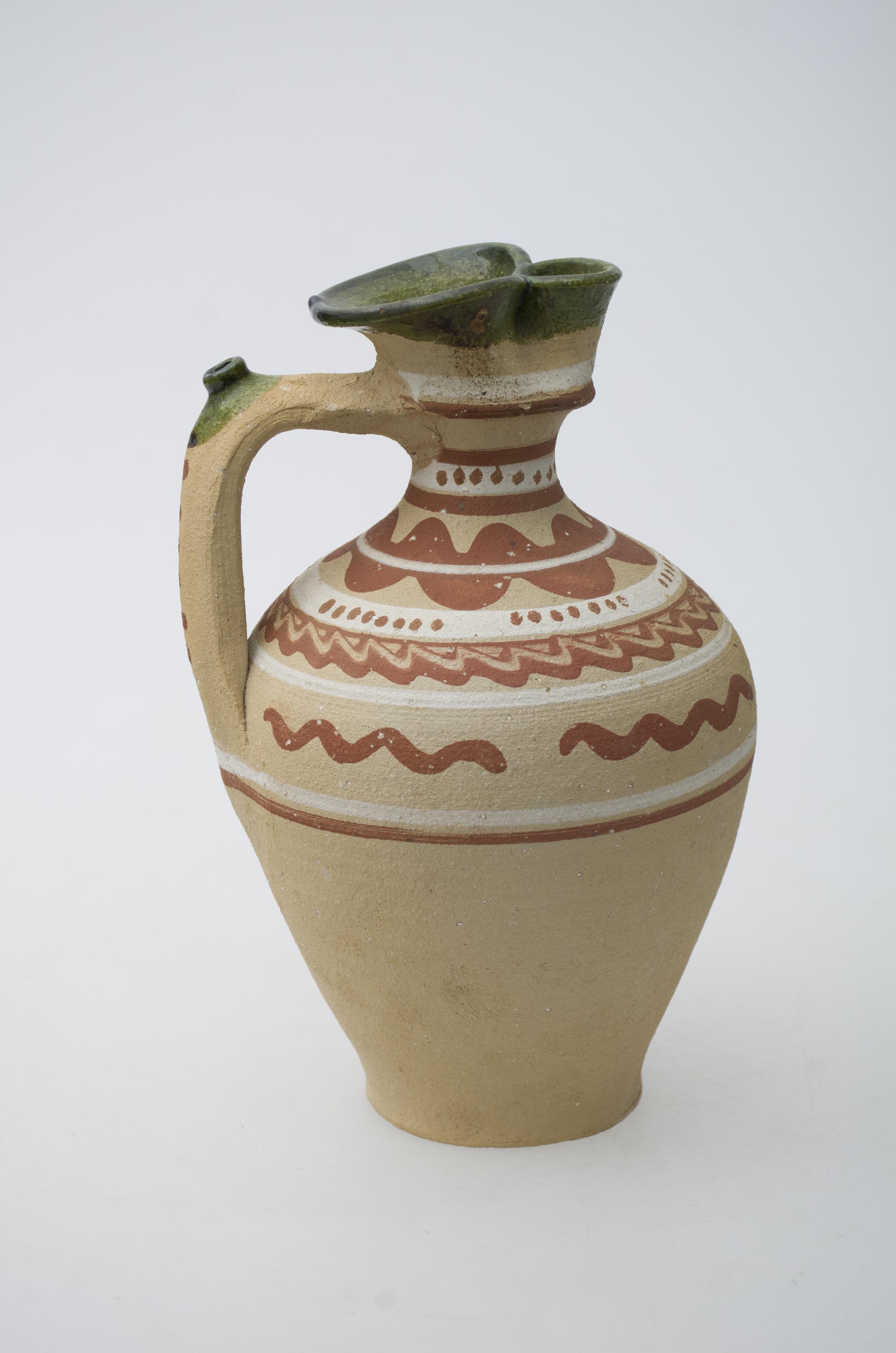 Vas ceramic, de formă bitronconică, cu baza plată, gâtul înalt și gura bilobată. Ulciorul prezintă o toartă cu ”țâță”, care pornește din zona gâtului și se unește cu vasul în zona diametrului maxim. Umerii, gâtul și buza recipientului ceramic prezintă decor geometrizant: un registru pictural, compus din linii concentrice, urmate de linii vălurite. Umerii ulciorului au fost decorați cu o linie groasă vălurită, buza și partea superioară a toartei fiind ornamentate la rândul lor, cu vopsea de culoare verde. Pe fund a fost imprimat textul: „IONICĂ STEPAN. BINIȘ”. Prezintă uzură funcțională. Cromatică: fond: cărămiziu deschis; motive: alb, maro roșcat, verde.