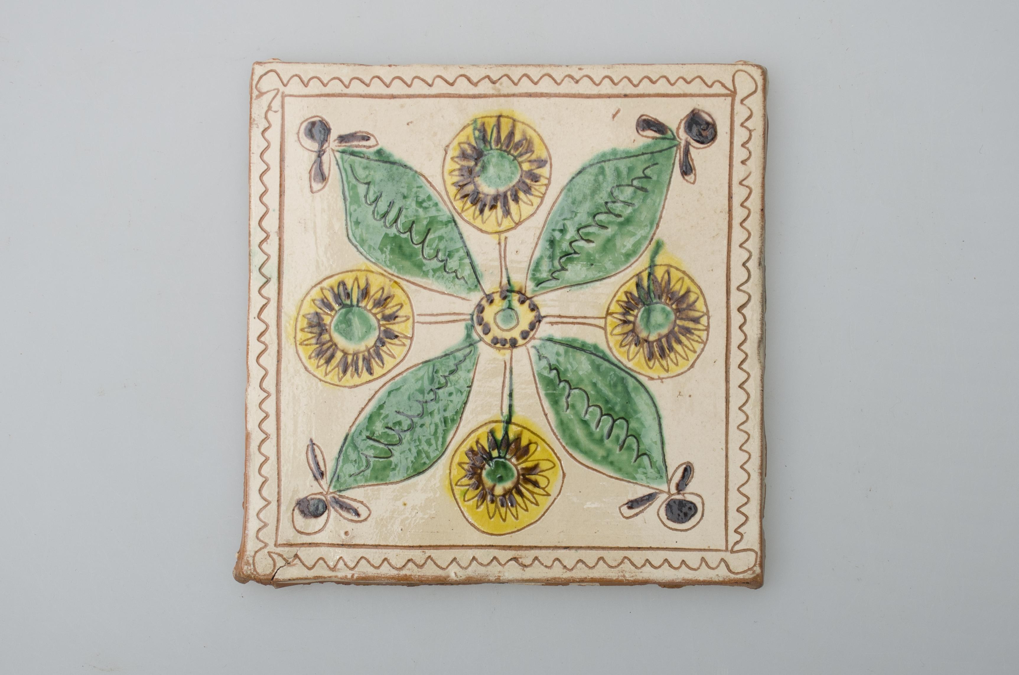 Piesă ceramică de formă pătrată, smălțuită și angobată, cu rol decorativ. Laturile pătratului sunt marcate de două chenare, primul vălurit, al doilea în linie dreaptă. Ornamentată cu motive vegetal-florale: patru flori care alternează cu patru frunze, având toate în comun un cerc, la mijlocul plăcii. Motivele au fost la început incizate, iar apoi pictate. Pe spate, cahla este prevăzută cu un orificiu pentru prinderea aței. Tot aici, este inscripționat numele meșterului olar, "Colibaba". Cromatică: fond: alb; motive: verde, galben, maro, negru.