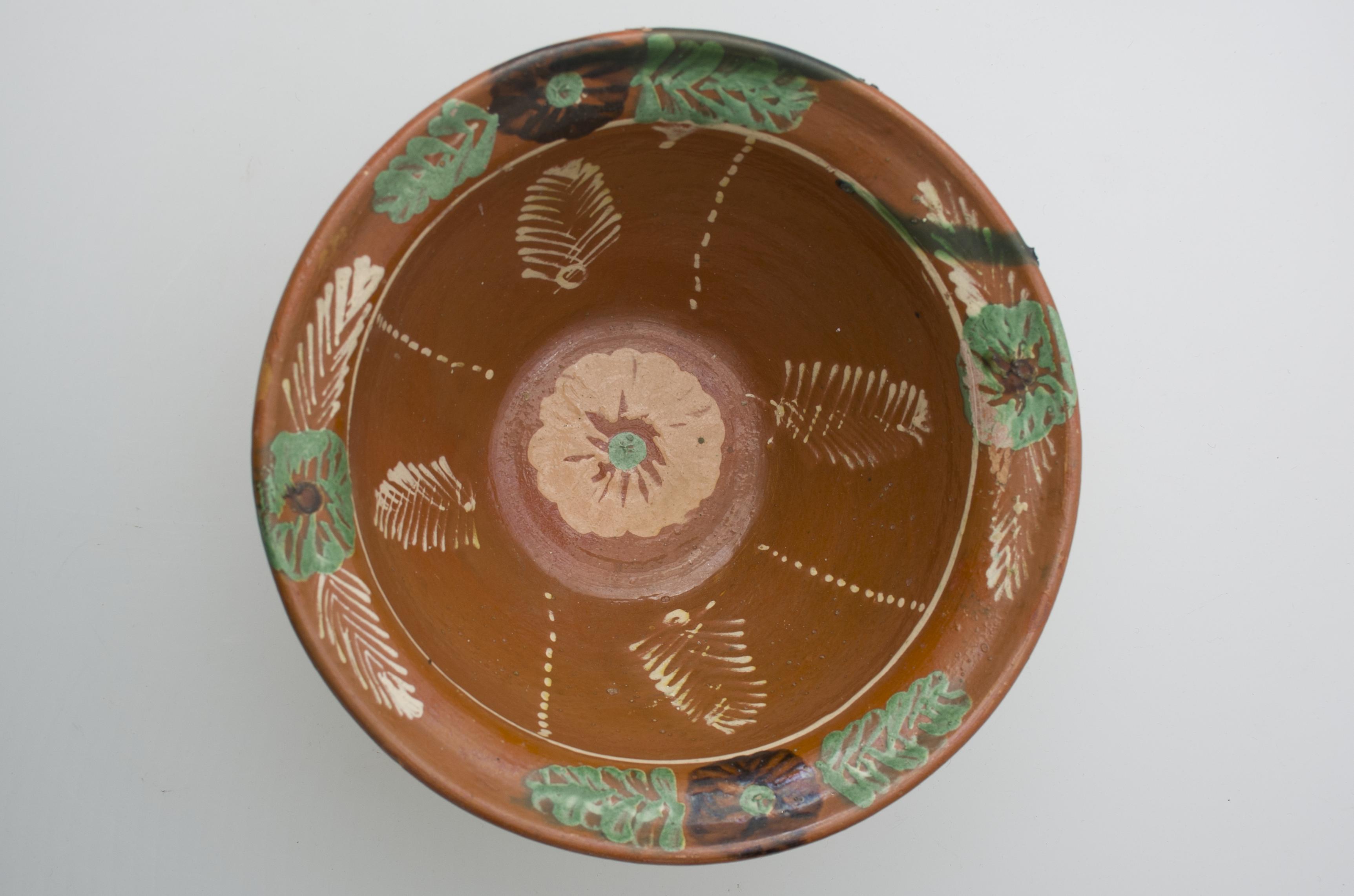 Recipient ceramic smălțuit,de formă tronconică, având pereții înalți și ușor evazați, baza plată și buza circulară. Decorat cu motive vegetale, florale și geometrice pe toată suprafața vasului: central o floare, șiruri de puncte și frunze pe pereți și flori și frunze, pe marginea gurii. Cromatică: fond: cărămiziu; motive: alb, verde, maro, crem.