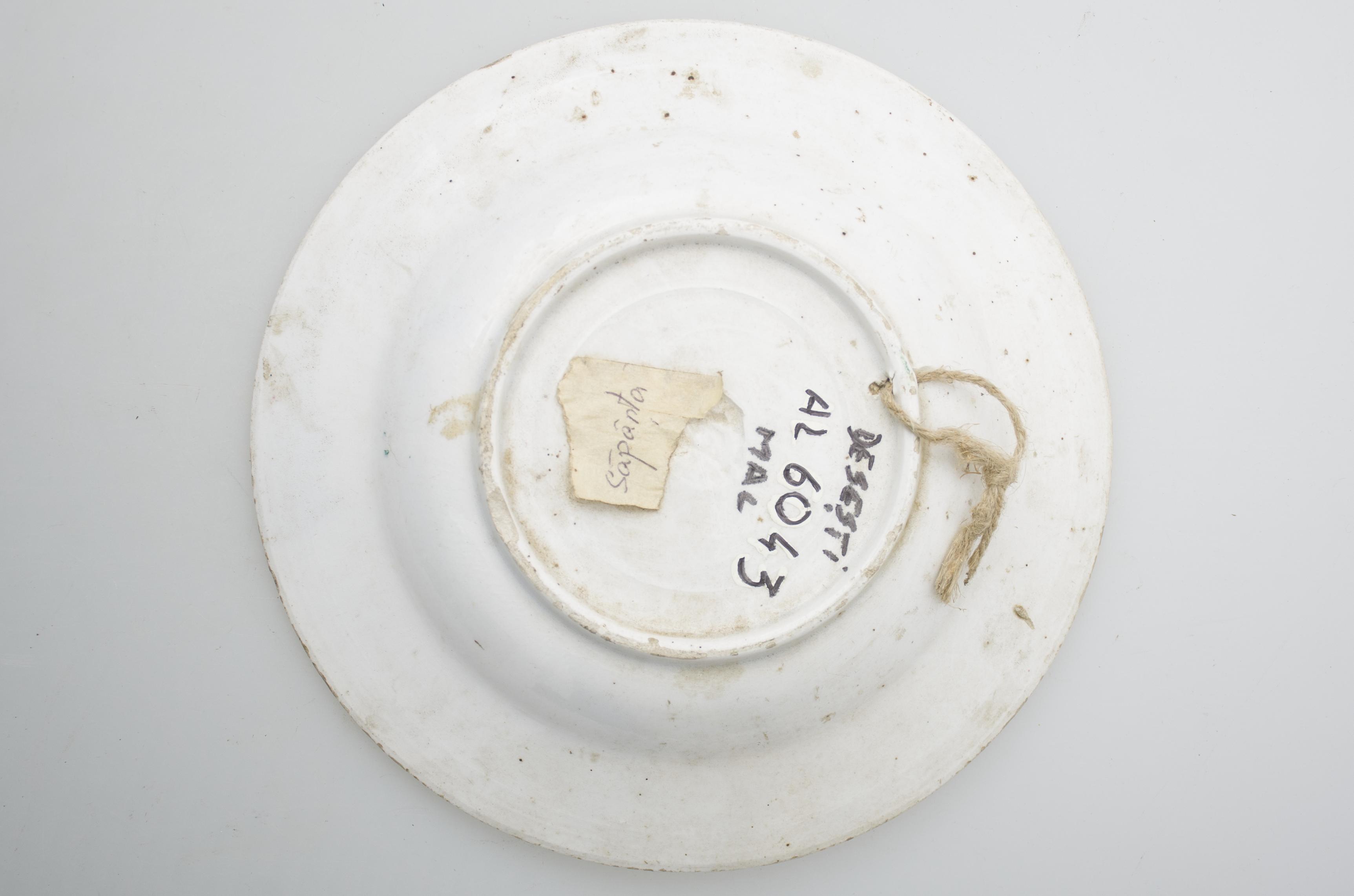 Vas ceramic de formă rotundă cu marginile puțin ridicate și fundul plat. Pe fond alb decorare cu motive floral-vegetale pe toată suprafața fundului vasului. Sunt ilustrate în plan central câte două flori roșii și două flori albastre cu o bulină galbenă în mijloc, încadrate de frunze verzi și albastre, tulpini maron și alte trei flori roșii de mici dimensiuni. Pe buza vasului două linii, în negru și maron, concentrice, iar pe margine șir de triunghiuri roșii de mici dimensiuni cu vârful spre interior. Baza vasului plata, cu inel de sustinere. Prevăzut cu "urechi" de susținere pentru agățare. Cromatica: fond: alb; motive: roșu, albastru, verde, galben, maro, negru.