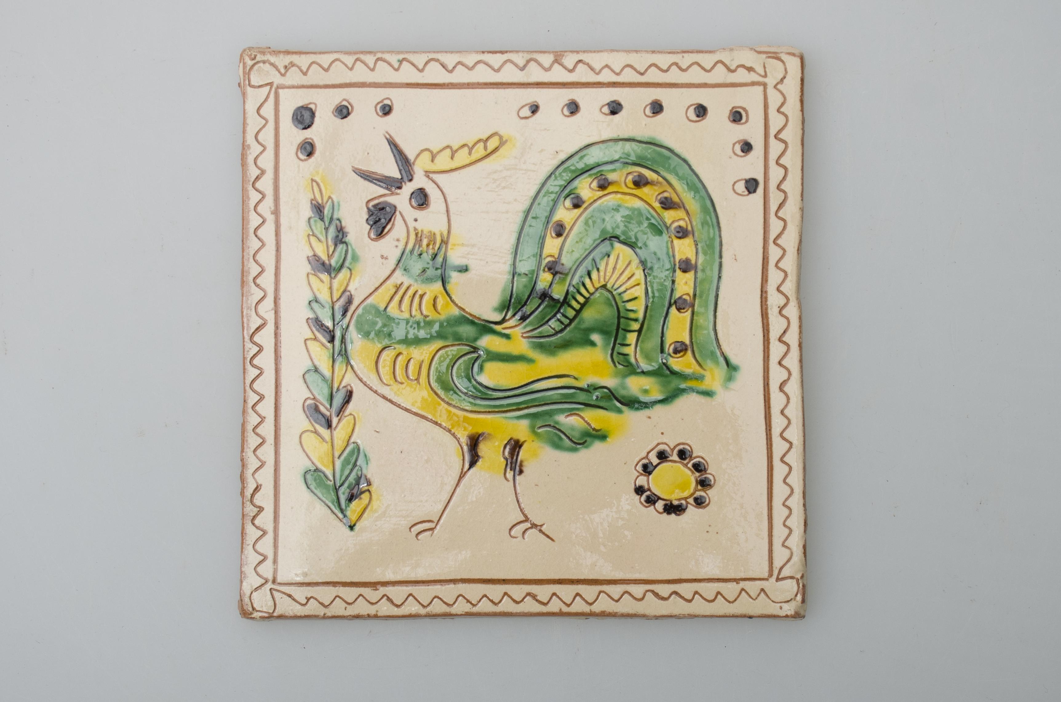 Piesă ceramică de formă pătrată, smălțuită și angobată, cu rol decorativ. Laturile pătratului sunt marcate de două chenare, primul vălurit, al doilea în linie dreaptă. Ornamentată cu motive avimorfe, vegetal-florale și geometrice: un cocoș cu pliscul deschis privește în sus, spre stânga. Este încadrat de două flori diferite și de un șir întrerupt de puncte. Motivele au fost la început incizate, iar apoi pictate. Pe spate, cahla este prevăzută cu un orificiu pentru prinderea aței. Tot aici, este inscripționat numele meșterului olar, "Colibaba". Cromatică: fundal alb; motive: verde, galben, maro, negru.