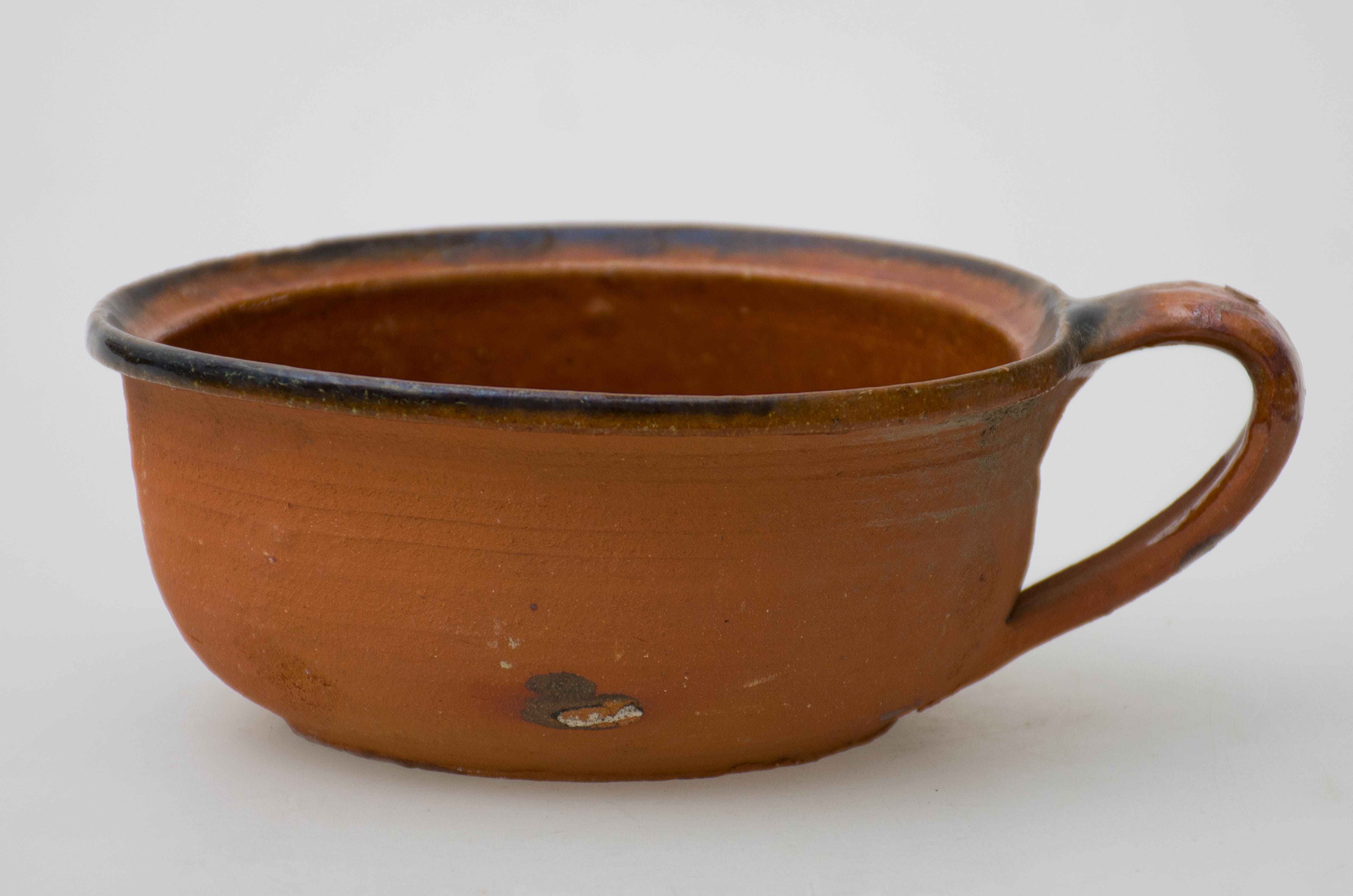 Vas ceramic de formă tronconică și buza răsfrântă spre exterior. Prezintă un mâner tubular scurt. Pe fund, pictat în puncte galbene avem o spirală și o pată verde scursă. Smălțuit pe buză și pe întreaga suprafață interioară. Cromatică: fond: cărămiziu (exterior) și maro (interior); motive: galben, verde.