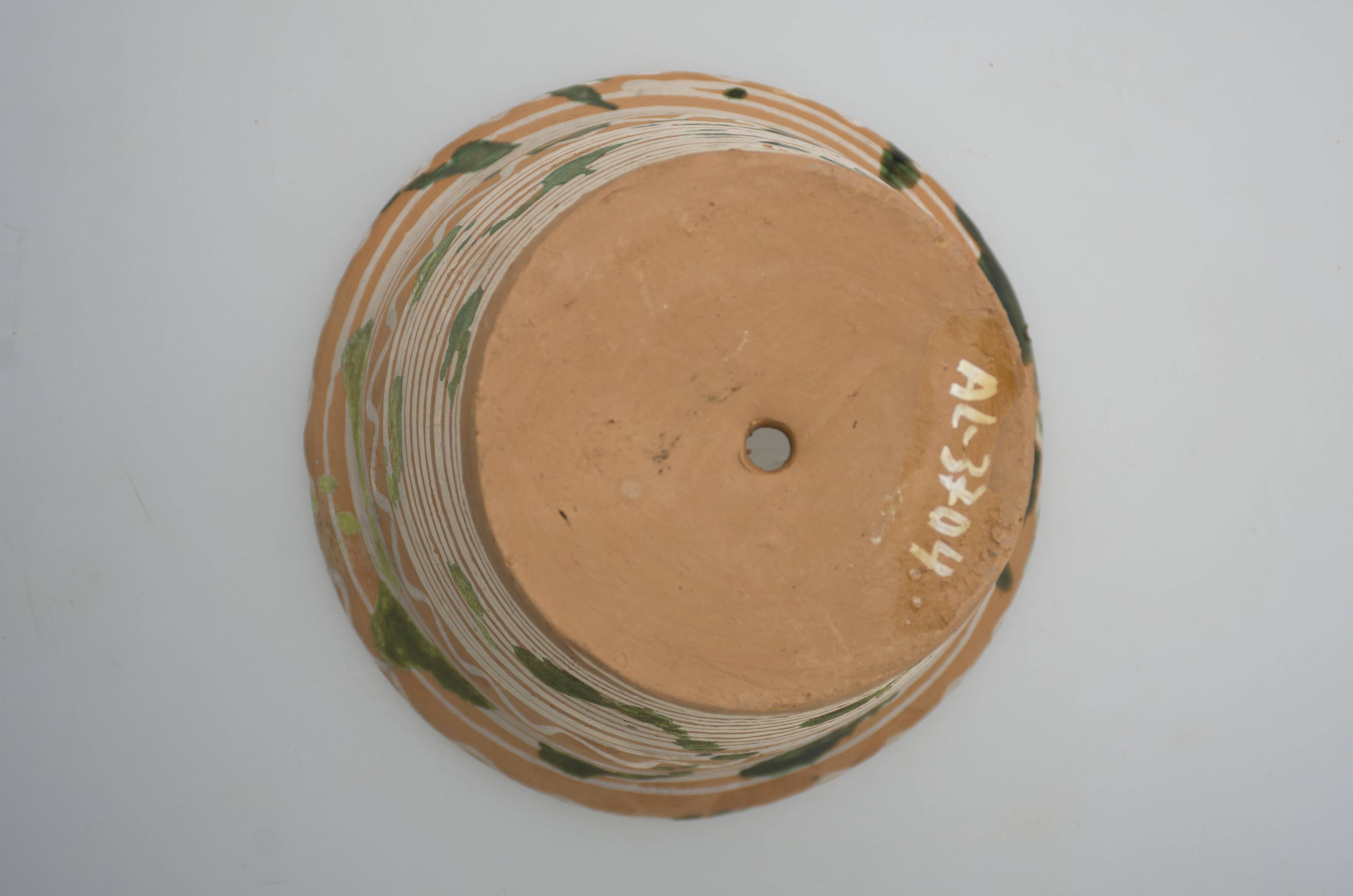 Vas ceramic de uz casnic, cu rol decorativ, întrebuințat în gospodărie ca ghiveci pentru flori. Recipient de formă tronconică, cu gura mai largă decât baza, cu buza ușor răsfrântă în exterior și rotunjită. Pe exteriorul vasului se identifică un decor pictat, realizat cu pensula, dispus în două registre. Decorul constă din motive geometrice care redau cercuri concentrice și linii vălurite. Peste decorul pictat a fost aplicat un decor realizat prin stropire, cu motive constând din pete verzi. Baza este prevăzută cu orificiul pentru scurgerea apei. Vasul a fost ars în tehnica arderii oxidante. Cromatică: fond: cărmiziu; motive: alb; verde.