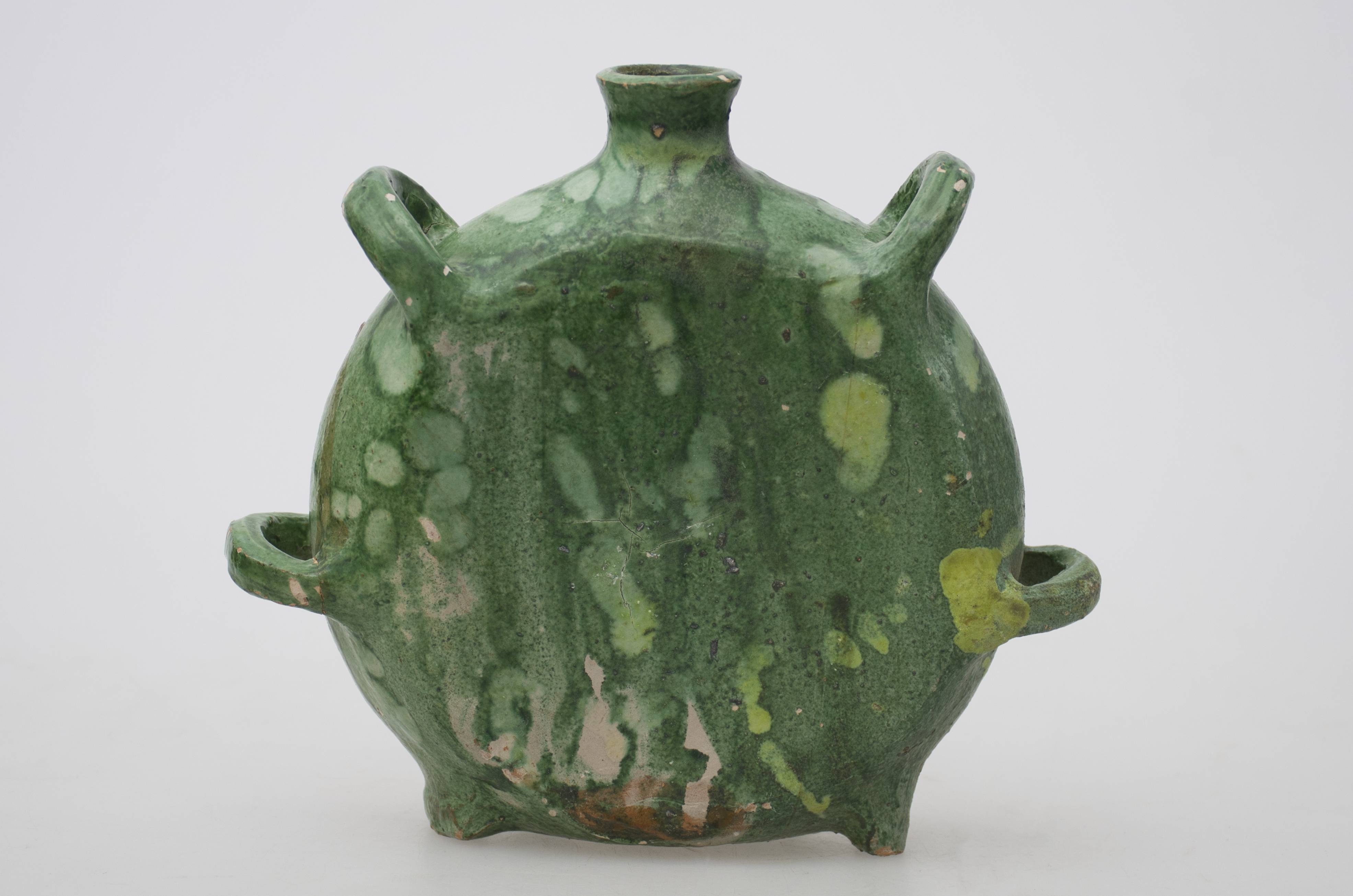 Vas ceramic de uz casnic, întrebuințat în gospodărie la stocarea și servirea lichidelor. De formă circulară cu ambele fețe plate având în partea inferioară două picioare de susținere iar la diametrul maxim două inele de prindere. De o parte și de alta a gâtului se repetă inelele de prindere. În partea superioară este gâtul înalt și subțire și cu gura ale cărei buză este rotunjită. Angobat, colorat în verde și smălțuit. Cromatică: fond: verde; motive: pete de culoare verde.