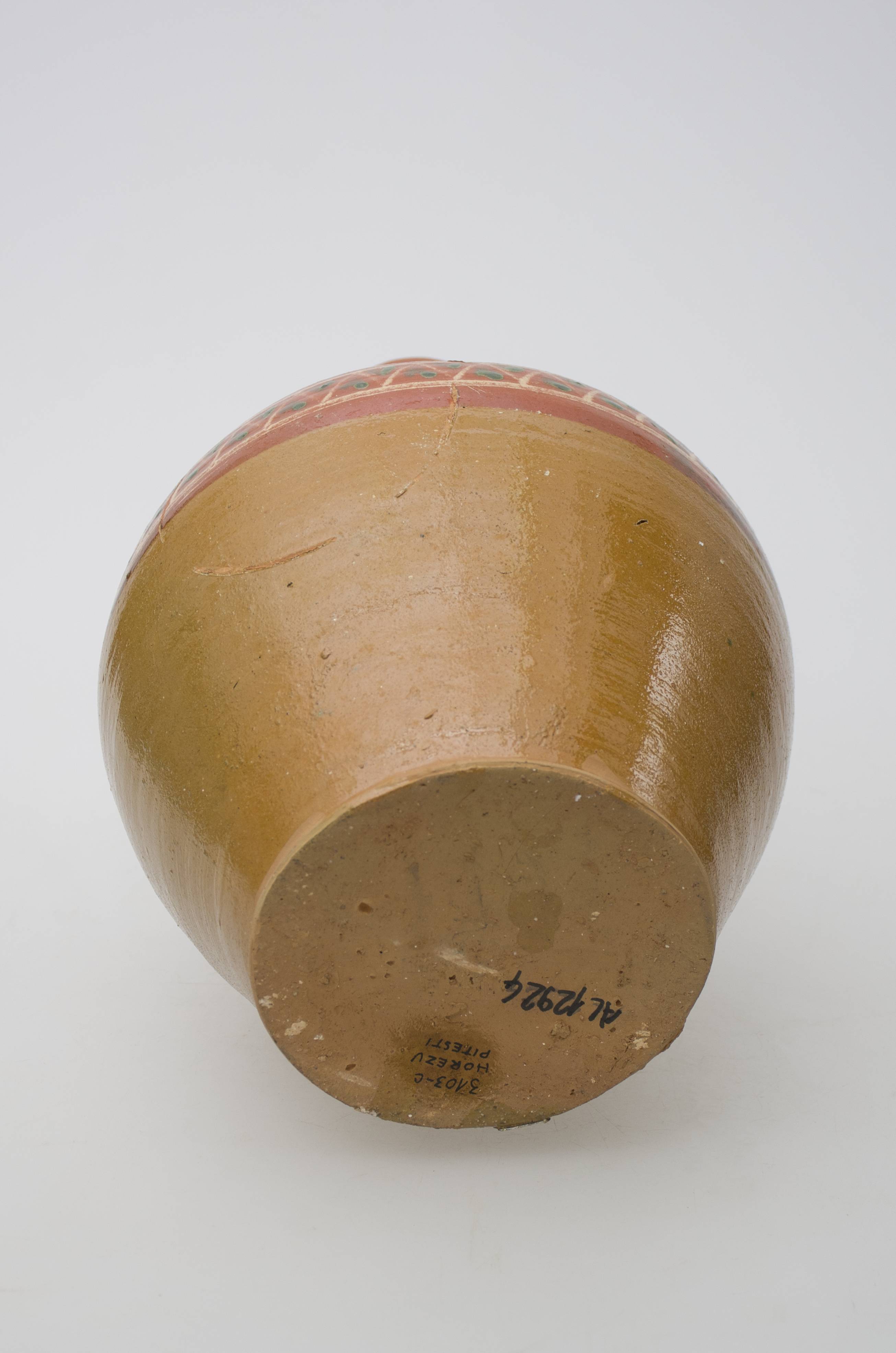 Vas ceramic de uz casnic, întrebuințat în gospodărie la stocarea, servirea și transportul lichidelor sau ca și element decorativ. Recipient de formă bitronconică, cu corpul globular, cu gâtul îngust și lunguieț. Gura este o prelungire a gâtului și are buza evazată, inelară, îngroșată și rotunjită. Ulciorul este prevăzut cu o toarta cu țâță care este dipusă între gât și jumătatea recipientului. Vasul este ornamentat prin pictare. Decorul este dipus pe jumătatea superioară a vasului, până sub gât și cuprinde motive geometrice și inscrpiții după cum umrează: două cercuri concentrice paralele care incorporează o linie frântă și puncte; inscripiția: "Din Călimănești. 1960". Deasupra inscripției se identifcă puncte/pete verzi și albe realizate cu pensula. Vasul este smălțuit până la fund. Cromatică: fond: roșu-cărămiziu; toarta: brun închis; partea inferioară: ocru; motive: alb; alb-gălbui; verde.