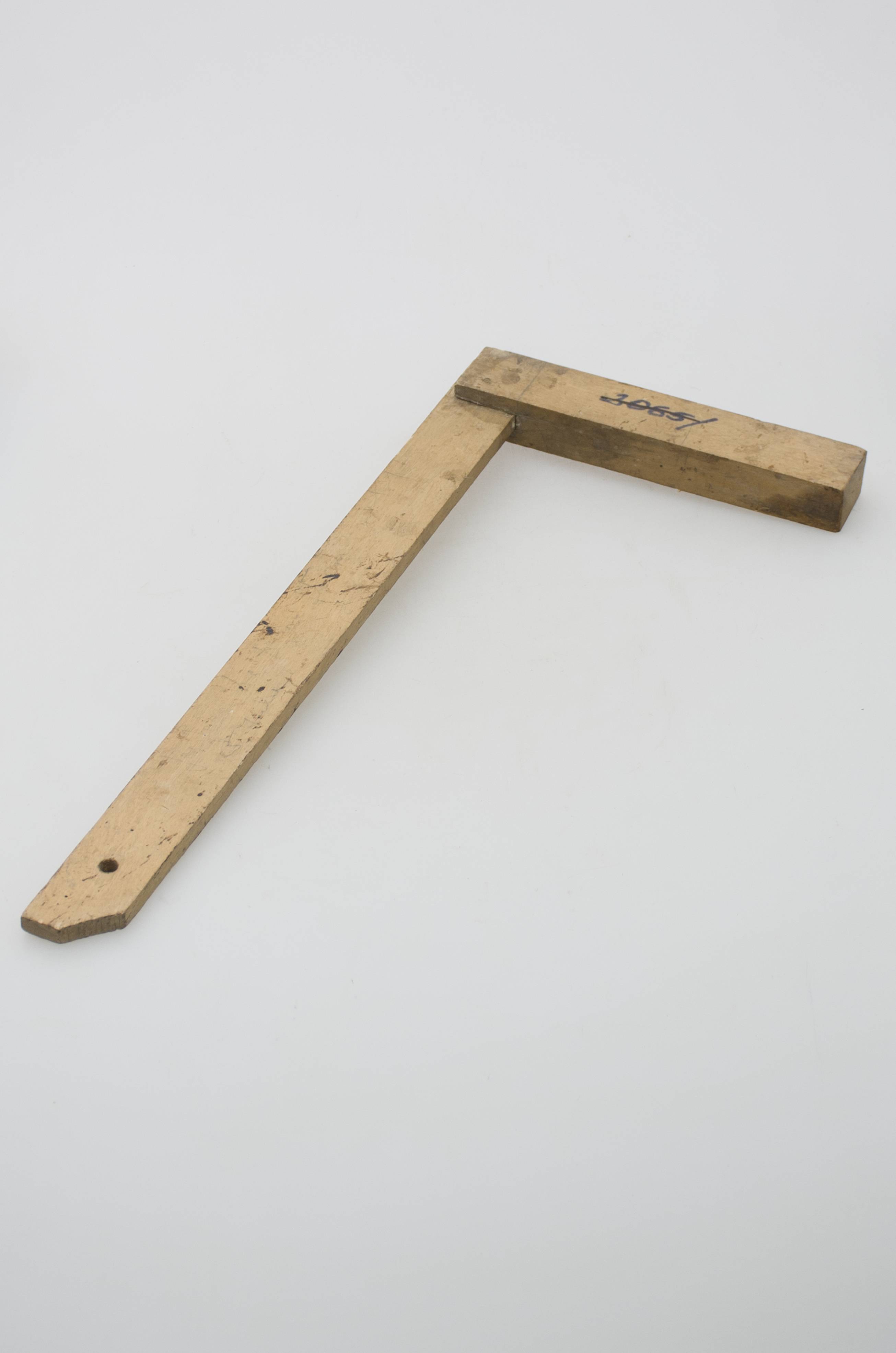 Obiect din lemn de esență tare compus din două stinghii înguste și îmbinate una cu alta la un capăt ca să formeze un unghi de 90 grade, fixate prin două cuie metalice. Vârful prezintă un orificiu pentru agățare / depozitare având unul dintre colțuri tăiat la 45 de grade. Unealtă de uz meșteșugăresc folosită în atelierele de tâmplărie / dulgherie la prelucrarea lemnului. Cromatică: culoarea patinată a lemnului; prezintă uzură funcțională.