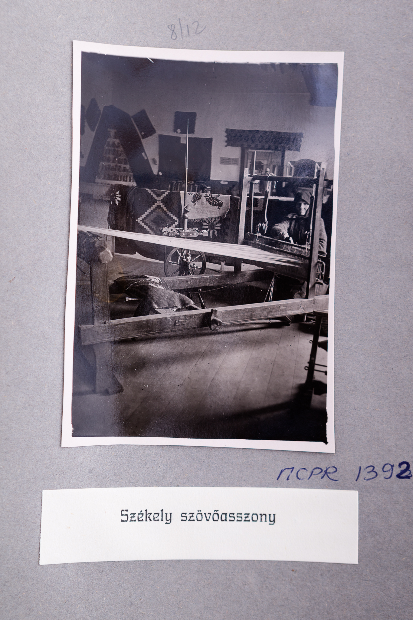 Fotografia de interior realizată în expoziția permanentă a Muzeului Secuiesc din Șumuleu Ciuc (actualmente cartier al localității Miercurea Ciuc), județul Harghita. Imaginea este imprimată pe hârtie fotografică cu gelatino-bromură de argint (Gelatin Silver Print). Reprezintă o femeie în costum popular secuiesc, lucrând la un război de țesut. Se remarcă războiul orizontal și textilele expuse pe pereții încăperii. Fotografia este lipită pe un carton gri, parte a albumului realizat în 1930. Acesta cuprinde imagini din expoziție și piesele expuse. Sub fotografie, număr de inventar MCPR 1392 și text în limba maghiară, imprimat pe o bucată de hârtie albă: „Szekely szövőasszony” (Țesătoare din secuime).