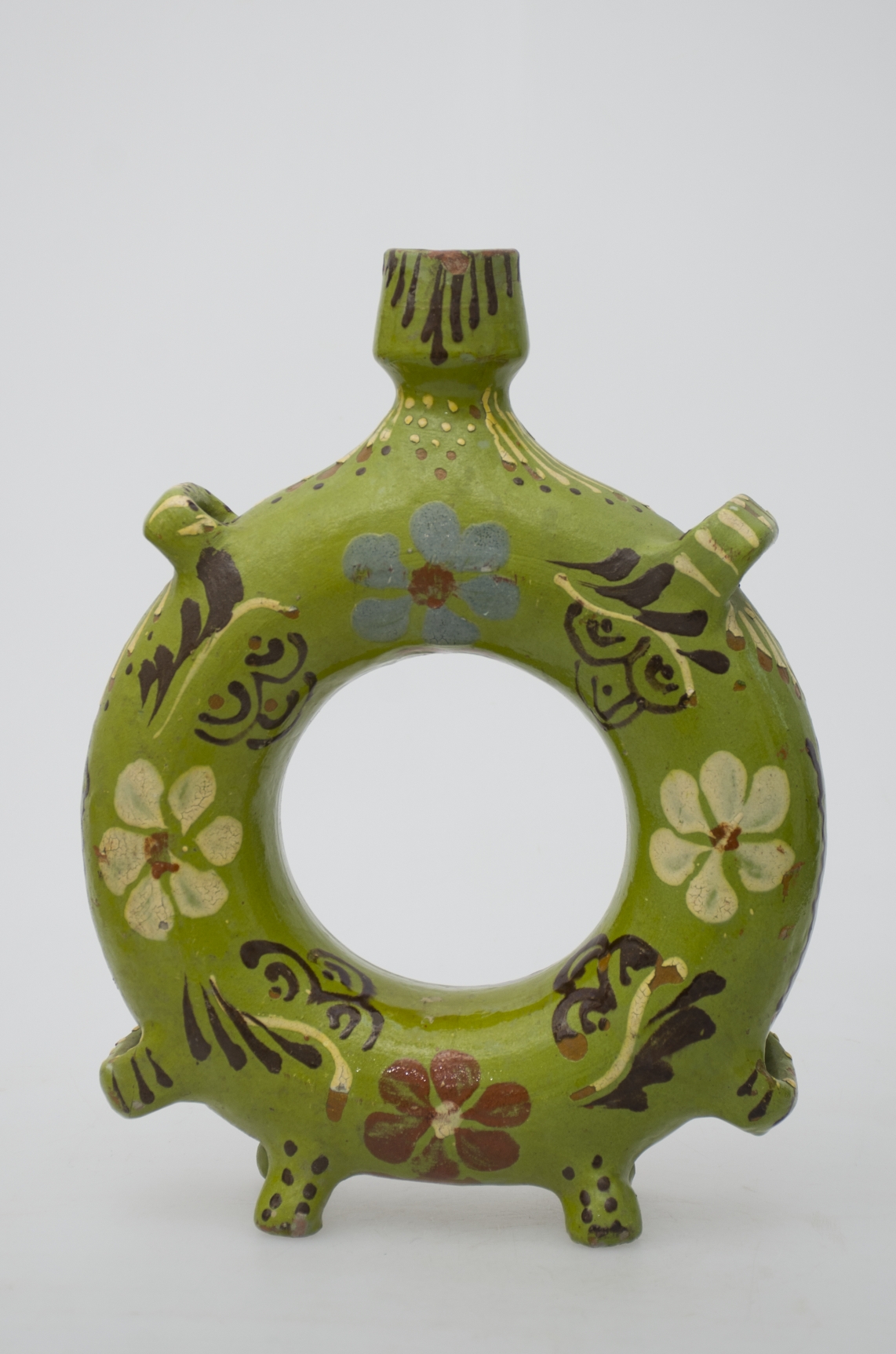 Ploscă ceramică cu corp inelar (toroidal); patru picioare; patru urechi; gură îngustă. Întreaga suprafață este ornamentată cu motive florale. Cromatica: fond verde deschis; motive alb; albastru; maron inchis; maron deschis.