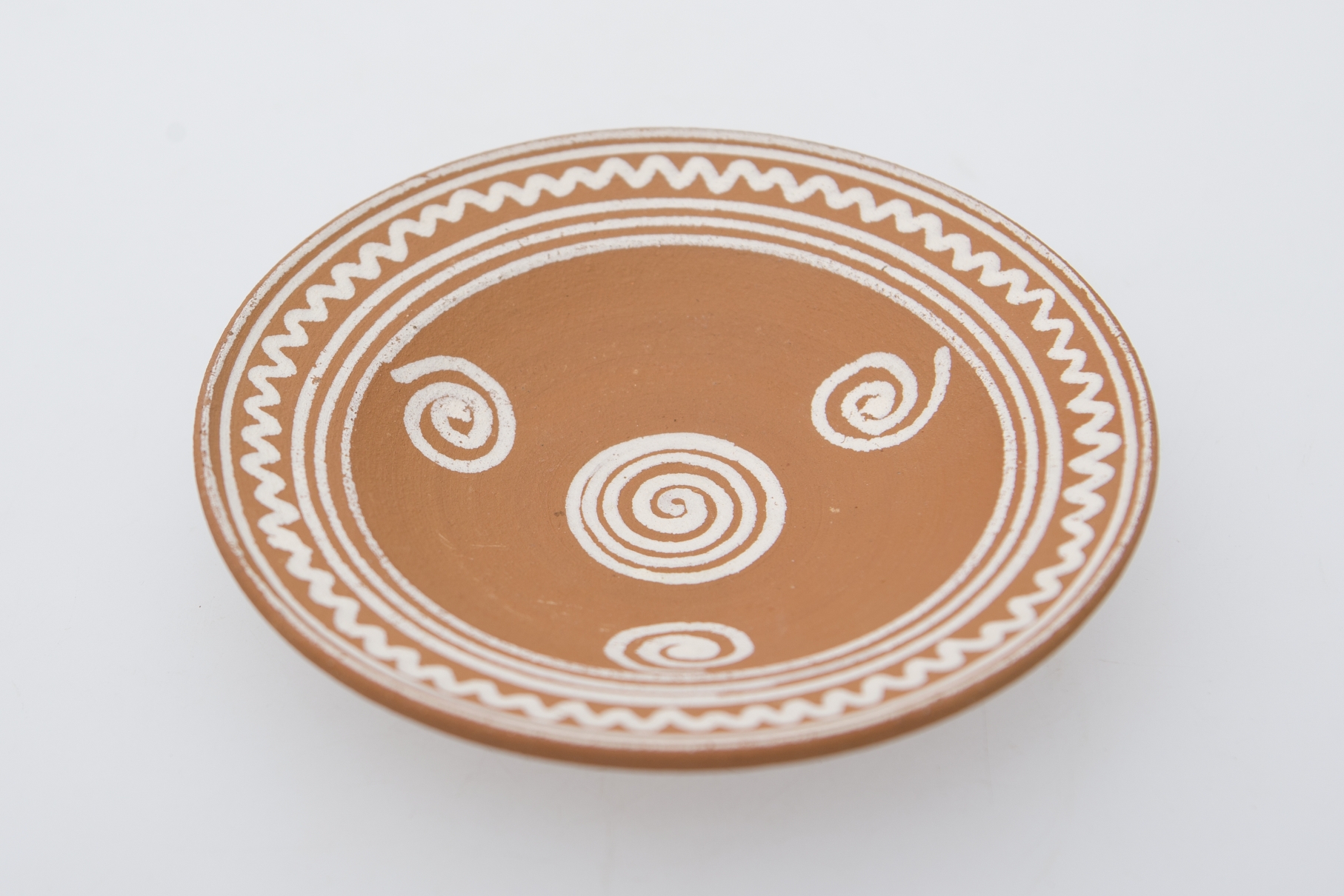 Vas ceramic de formă tronconică, pe bază inelară, fundul vasului puțin adâncit și plat, cu marginile puțin ridicate. Pe fundul farfuriei a fost pictată o spirală. Pe pereți alte trei spirale. Pe buza farfuriei trei cercuri se circumscriu urmate de val și alte două cercuri. Pe fundul vasului, la spate, ștanțat ”Șchiopu Vlădești 1979'' înscris într-un cerc. Pe inelul de susținere dispuse două orificii pentru atârnare. Cromatică: fond: maro; motive: alb.