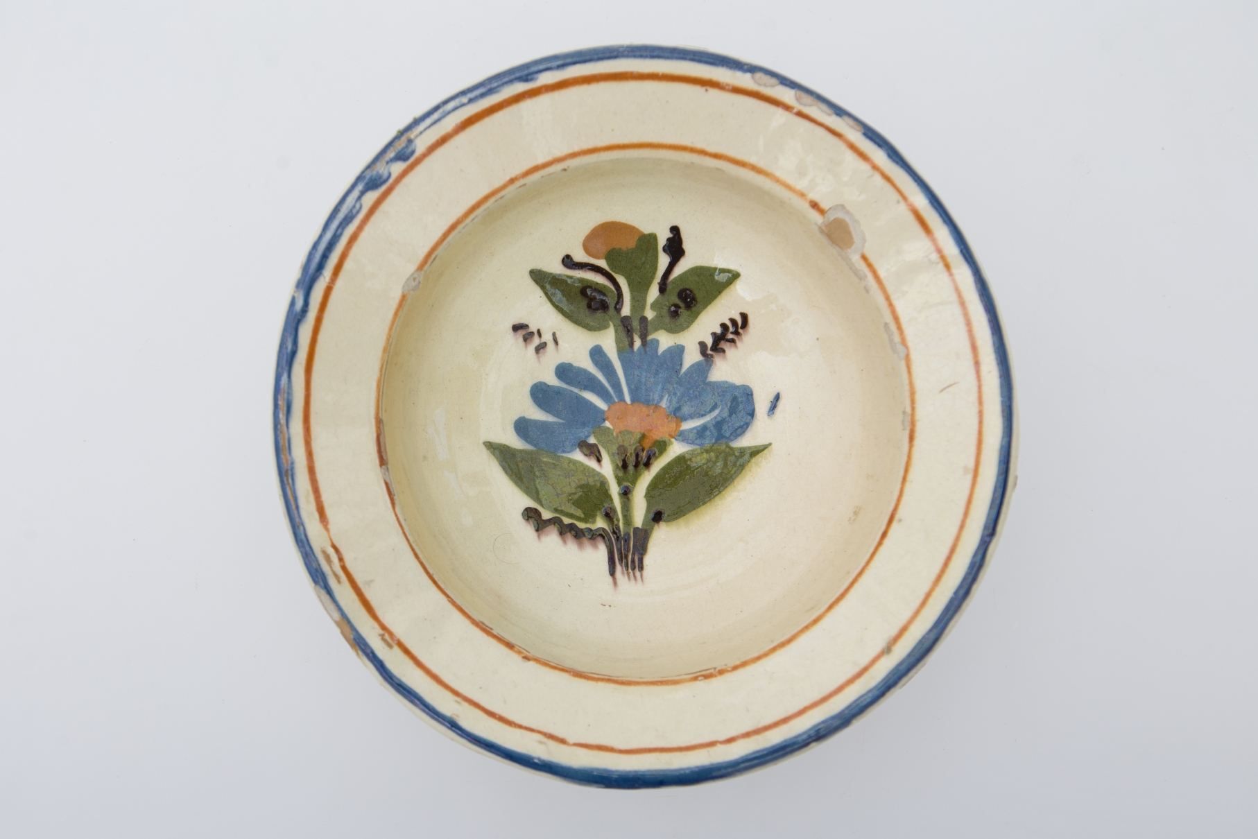 Farfurie de formă tronconică cu fundul plat, puțin adâncit. Pe fundul vasului decor ilustrând o floare cu petale albastre, maro în centru, frunze verzi, lujeri și tulpini maro închis. Marginea este delimitată de două linii maro circulare și buza conturată cu albastru. Cromatica: fond: alb; motive: albastru; verde; maro; maro închis.