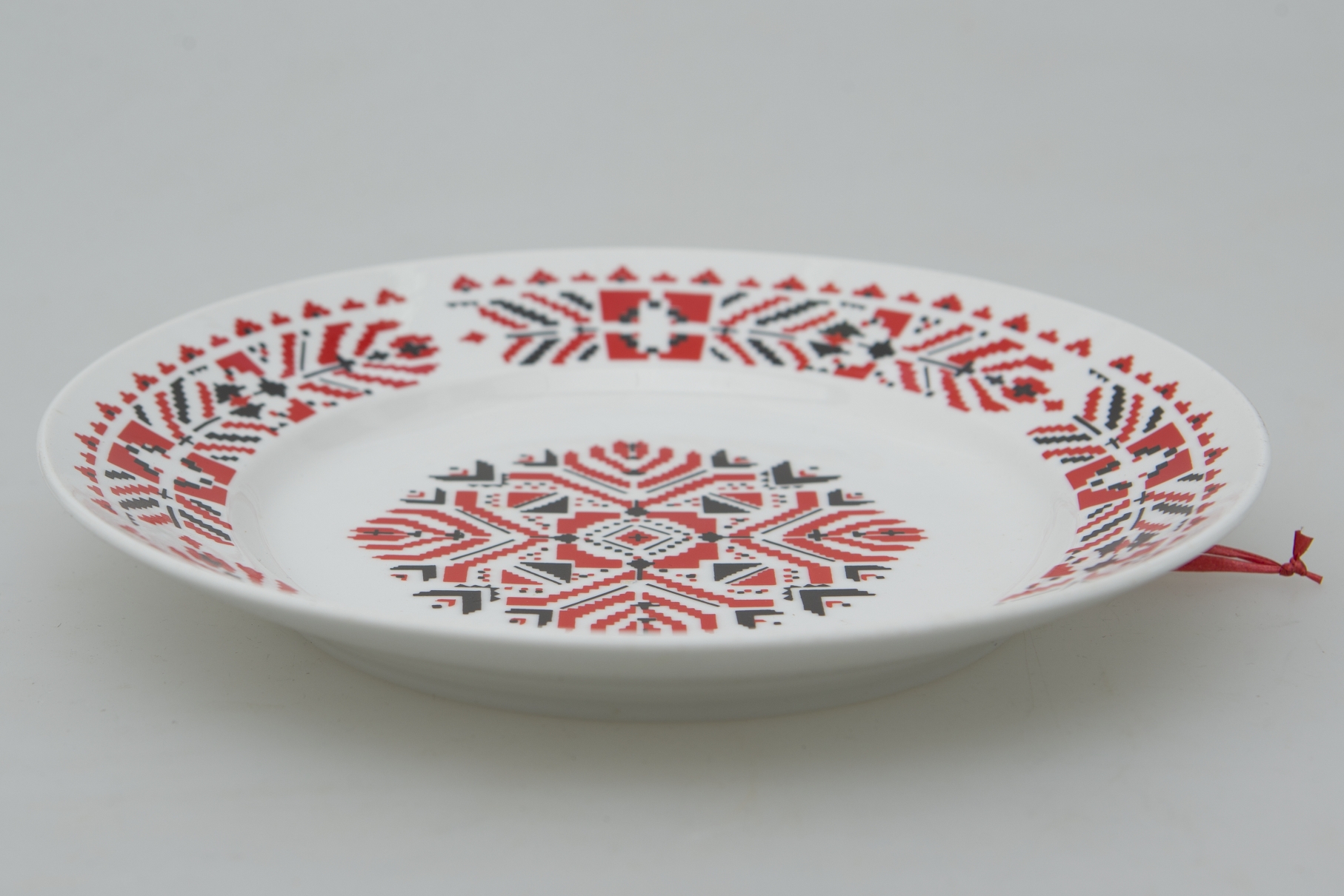 Farfurie de formă tronconică, ușor adâncită. Există două registre ornamentale, unul plasat de jur împrejurul buzei cu motive geometrice și florale stilizate. Al doilea registru plasat în centru cu același tip de motive. Smălțuit. Cromatică: fond: alb; motive: roșu; negru.