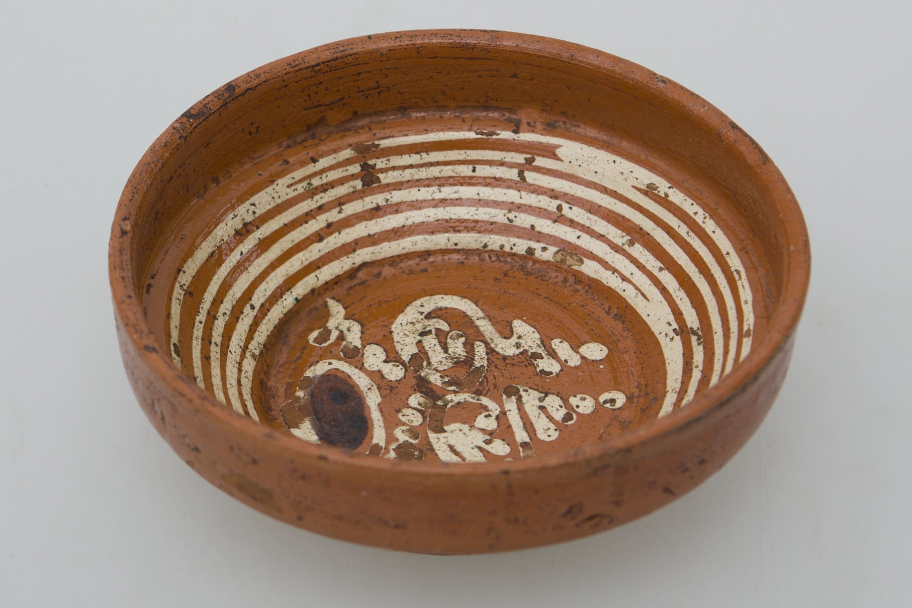 Vas ceramic de mici dimensiunui de formă tronconică cu marginea ușor evazată. Pe fundul vasului avem decorații floral-vegetale stilizate și pe pereții intreriori linii albe dispuse în cercuri concentrice. Cromatică: fond: cărămiziu; motive: alb.