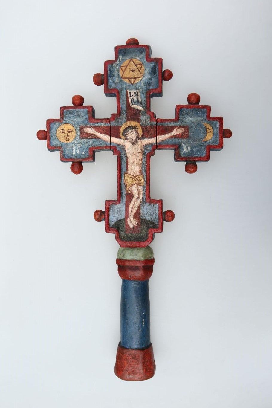 Obiect de cult confecționat din lemn de fag. Picturi deosebite pe cele două părți ale crucii. Pe o parte pe fond auriu este pictat Isus în poziție de rugăciune, încadrat de Sf. Ioan, în stânga, și un arhanghel în dreapta. Deasupra este pictat un porumbel simbolizând Sf. Duh. Pe cealaltă parte pe un fond de culoare albastră este ilustrat Isus răstignit încadrat de soare (în stânga) și lună (în dreapta), deasupra este pictat ochiul atotvăzător și steaua lui David. Marginile sunt pictate în albastru iar conturul în roșu. Pe o margine crucea este datată în anul 1806. În partea inferioară prezintă un orificiu în vederea introducerii unui suport. Prezintă 11 ornamentații sub formă de buton.