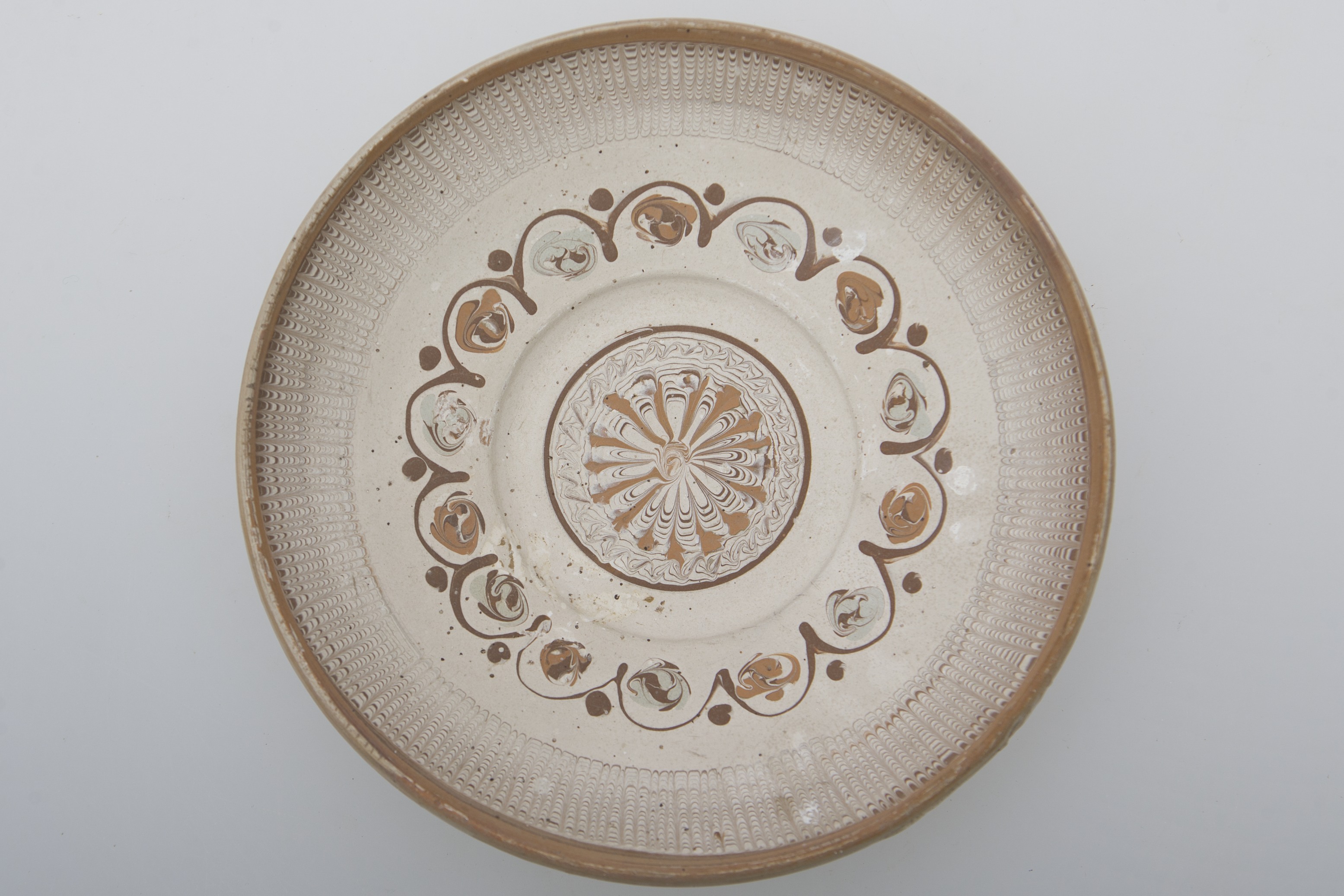 Vas de uz casnic, ceramic, de formă tronconică, ușor adâncit și buza rotunjită. Nesmălțuit și angobat. Prezintă decorații geometrice și florale pe întreaga suprafață interioară a vasului, realizate prin jirăvire cu gaița. În centrul vasului este redată o floare stilizată separată de restul vasului cu o linie circulară, maro. Pe pereți, decorul continuă cu o linie ondulată intercalată cu flori stilizate și puncte, apoi de benzi multiple, jirăvite. Prezintă urme de uzură funcțională. Cromatică: fond: alb, motive: negru; gri; maro deschis; maro închis.
