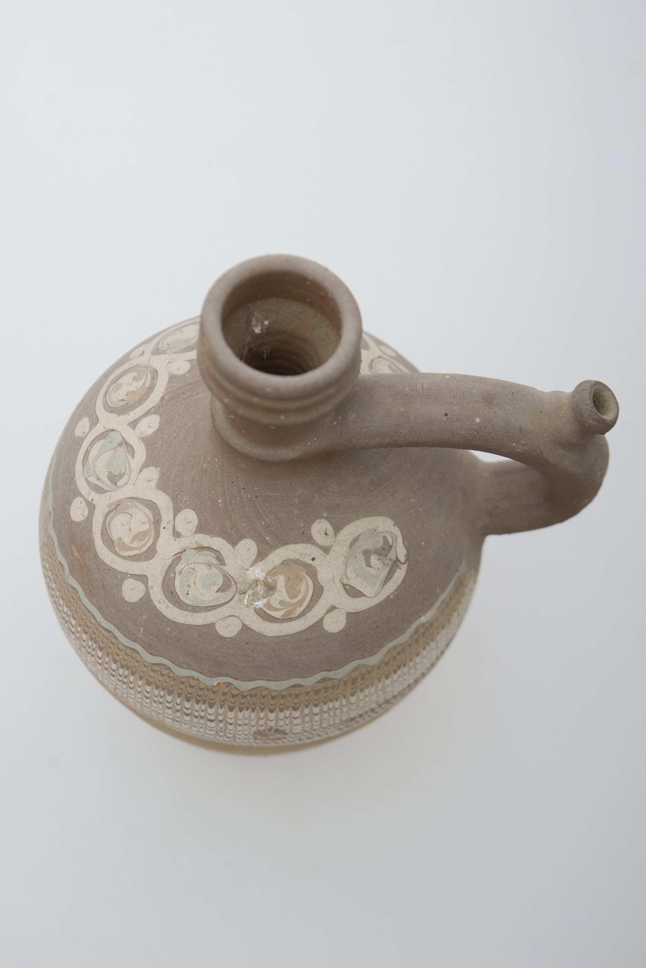 Vas ceramic, nesmălțuit, de formă sferoidală cu gât alungit care se termină cu o gură canelată și dreaptă. Prezintă o toartă arcuită prevăzută cu o țâță ce se prinde de gâtul piesei pe un inel în relief iar celălalt capăt de umărul acesteia. Decorul este dispus în zona mediană, ilustrând o bandă de flori stilizate pictate cu cornul urmate de benzi multicolore, jirăvite cu gaița. Cromatică: fond: cărămiziu; motive: alb; verde deschis; maro deschis; maro închis.