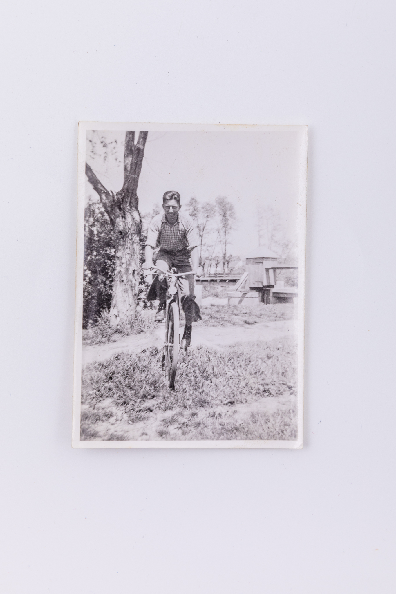 Fotografie de exterior, realizată pe malul unei ape, reprezentând un bărbat pe bicicletă. În plan secund se remarcă un pod din lemn. Hârtia folosită este Agfa Lupex, foarte populară până în anii 1945. Hârtie fotografică mată cu gelatino-bromură de argint. Pe verso marca Agfa Lupex; lipit număr inventar 3080 - CL.