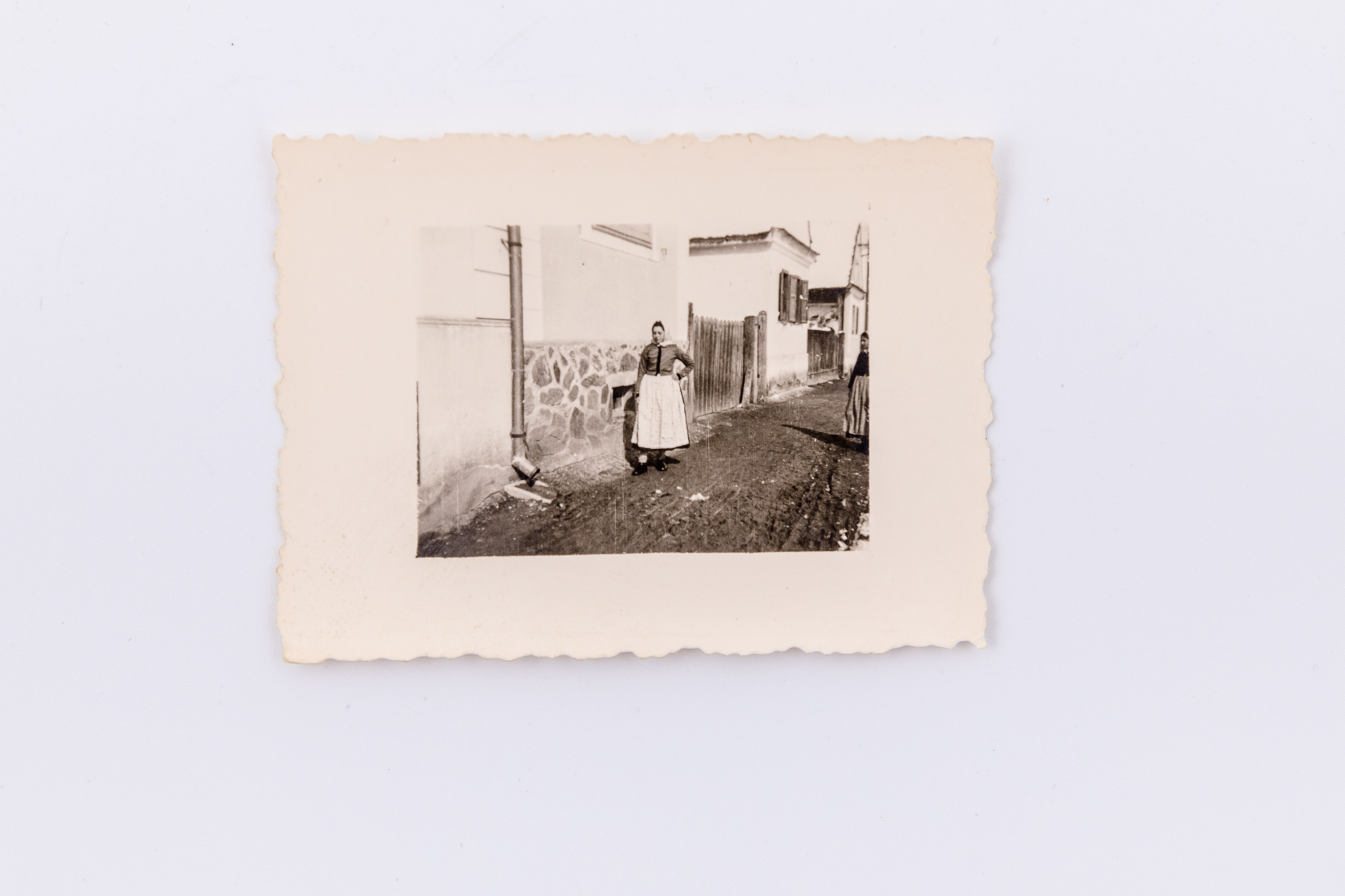 Fotografie de exterior ce prezintă o femeie îmbrăcată în costum de landleriță, pe stradă, lângă casă. Hârtie fotografică Agfa Lupex sensibilizată cu gelatino-bromură de argint, prin D.O.P. (developing-out paper – imprimare prin developare). Hârtia „Agfa Lupex” a fost foarte populară până în anul 1945. Marginile fotografiei sunt zimțate. Pe verso marca Agfa Lupex; lipit număr inventar 3055 - CL; Turnișor.