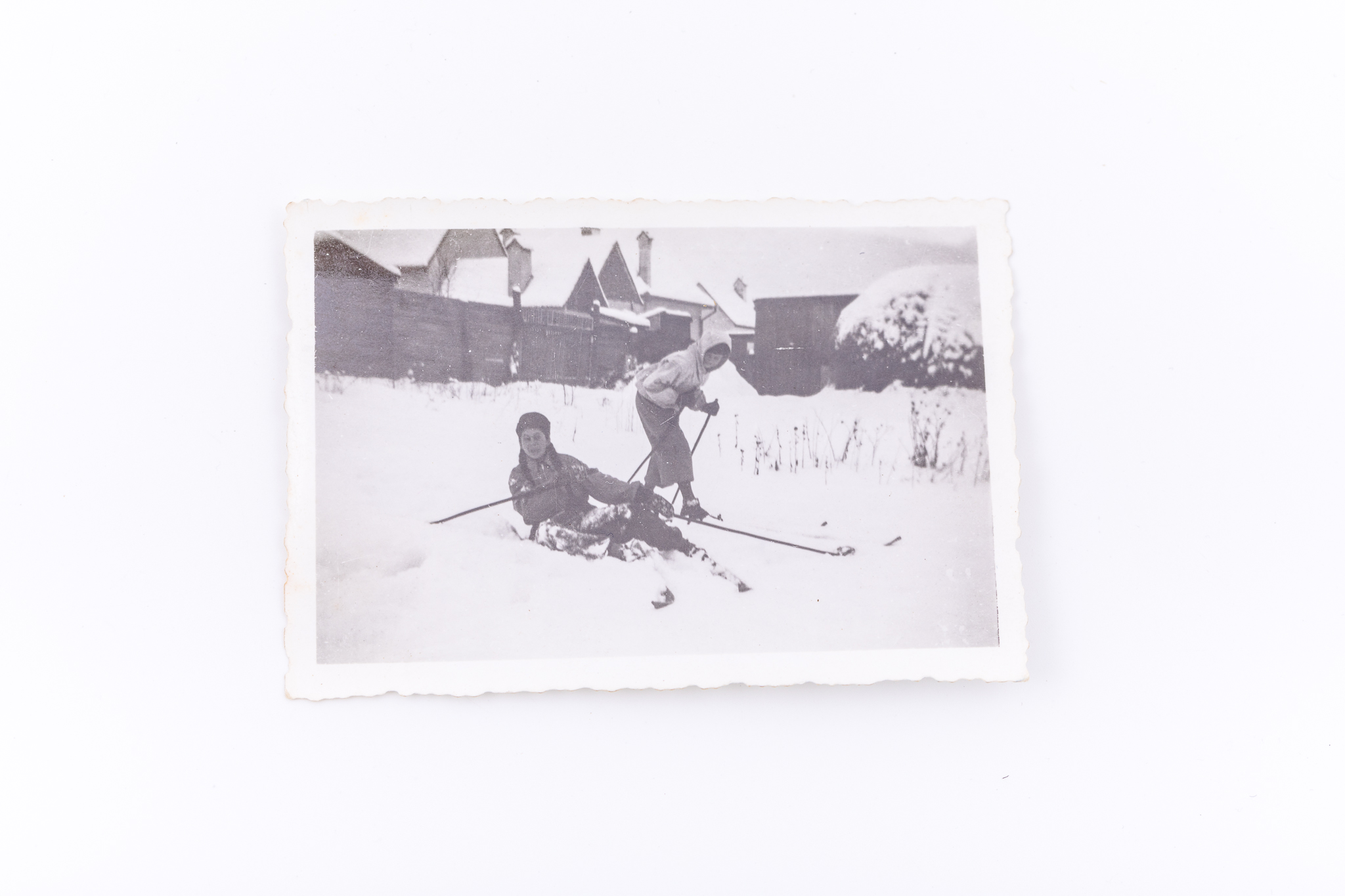 Fotografie de exterior realizată pe un câmp, în spatele unor case. Hârtie fotografică Agfa Lupex sensibilizată cu gelatino-bromură de argint, prin D.O.P. (developing-out paper – imprimare prin developare). Prezintă două fete pe schiuri. Hârtia „Agfa Lupex” a fost foarte populară până în anul 1945. Marginile fotografiei sunt zimțate. Pe verso marca Agfa Lupex; lipit număr inventar 3042 - CL, Turnișor.