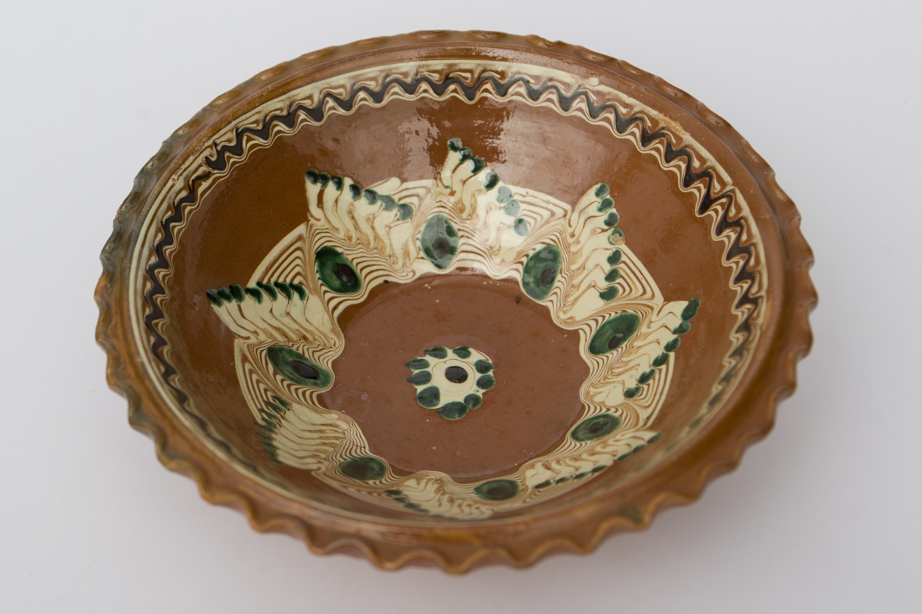 Vas ceramic smălțuit corp discoidal cu margini ridicate. Buza vasului ondulată prin impersiune cu degetetele. Decor geometrizant concentric. Pe fundul vasului amplasată o floare stilizată sugerată de un cerc punctiform suprapus pe o bulină albă, cu un punct în centru. Pe peretele interior un câmp jirăvit peste care se suprapun ”ochi de păun'' în alternanță cu ”creste de cocoș'', realizate prin scurgere cu cornul. Spre buză o bandă jirăvită peste care se suprapune o linie ondulată dispusă circular. La posterior baza perforată pentru atârnare și deaspura bazei incizat ”Colibaba''. Cromatică: fond: maro; motive: alb; verde; brun.