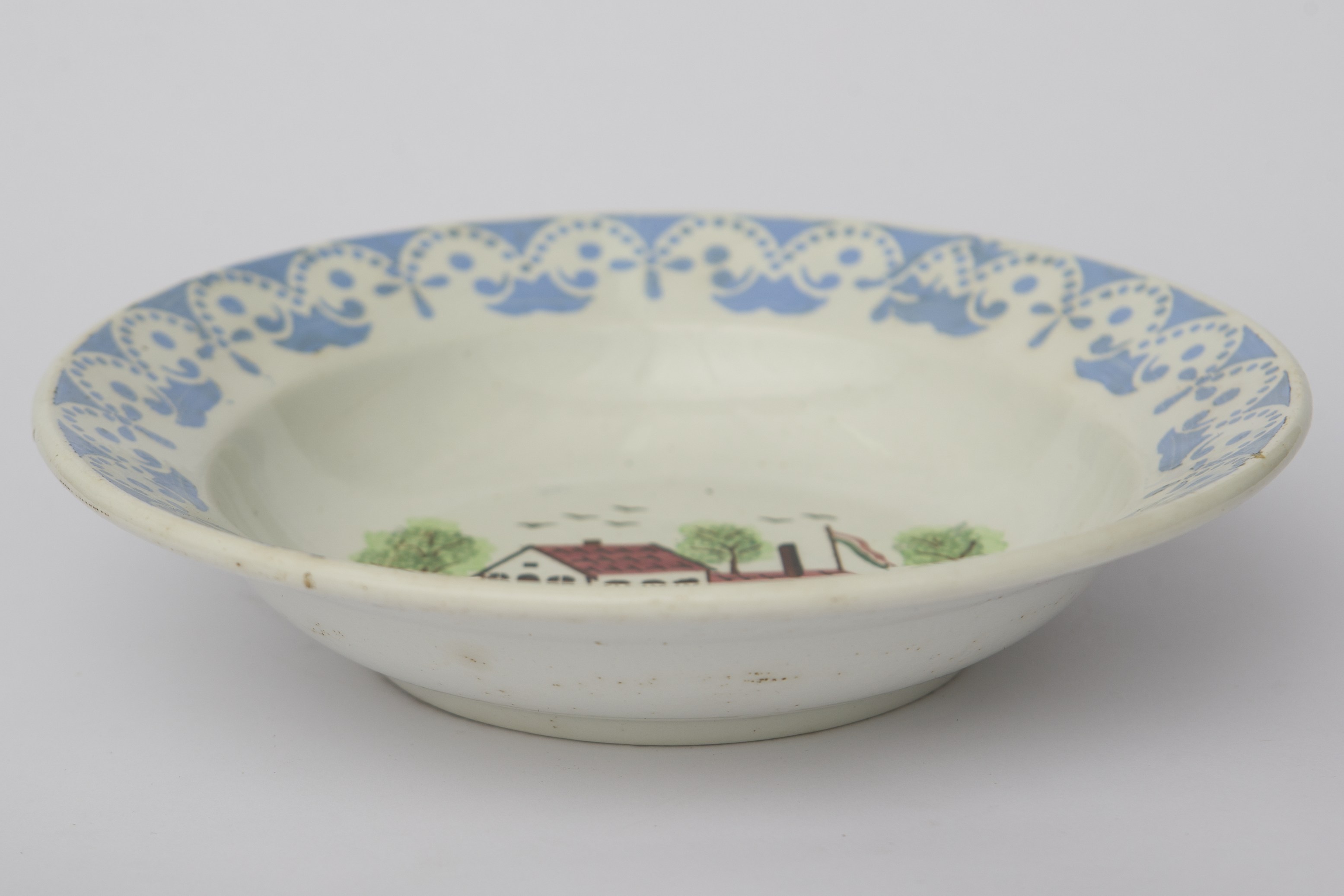 Vas ceramic de formă tronconică. Există două registre ornamentale, unul plasat de jur împrejurul buzei cu motive geometrice curbilinii: linii punctate; motive florale stilizate toate de culoare albastră. Al doilea registru plasat în centru reprezentând o gospodărie ce are pe fundal trei pomi și o fântână cu cumpănă în față. În partea dreaptă a gospodăriei este arborat un drapel (steagul Olandei). La posterior baza inelară perforată pentru atârnare. Cromatică: fond: alb; motive: verde; albastru; maro; roșu; galben; negru