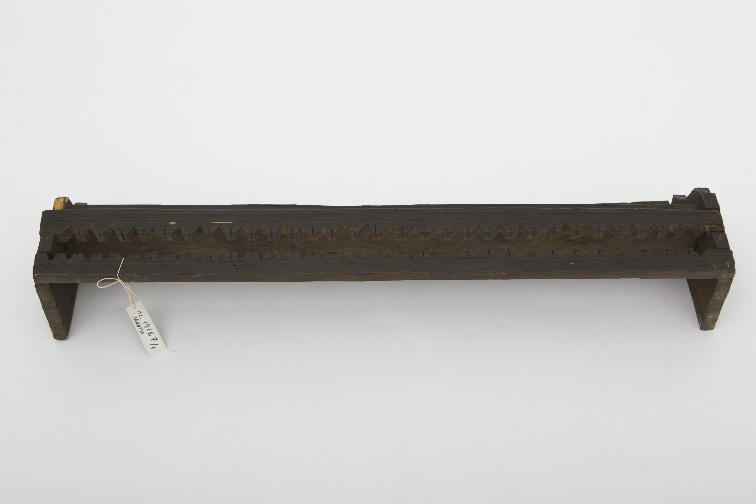 Piesă de mobilier de mici dimensiuni, realizată din lemn de brad și metal. Cuierul este format din două scânduri, fixate în formă de „L”, care prezintă la capete la capete alte două scânduri, reduse la dimeniuni, pentru întărire. Poliței i-au fost atașate frontal alte două scânduri încrustate. Decorul geometrizant simplist este format din încrustările în zig-zag, dispuse frontal. Cuierul era folosit în gospodărie pentru poziționarea vaselor ornamentale. Prezintă uzură funcțională. Cromatică: maro închis; culoarea patinată a lemnului.
