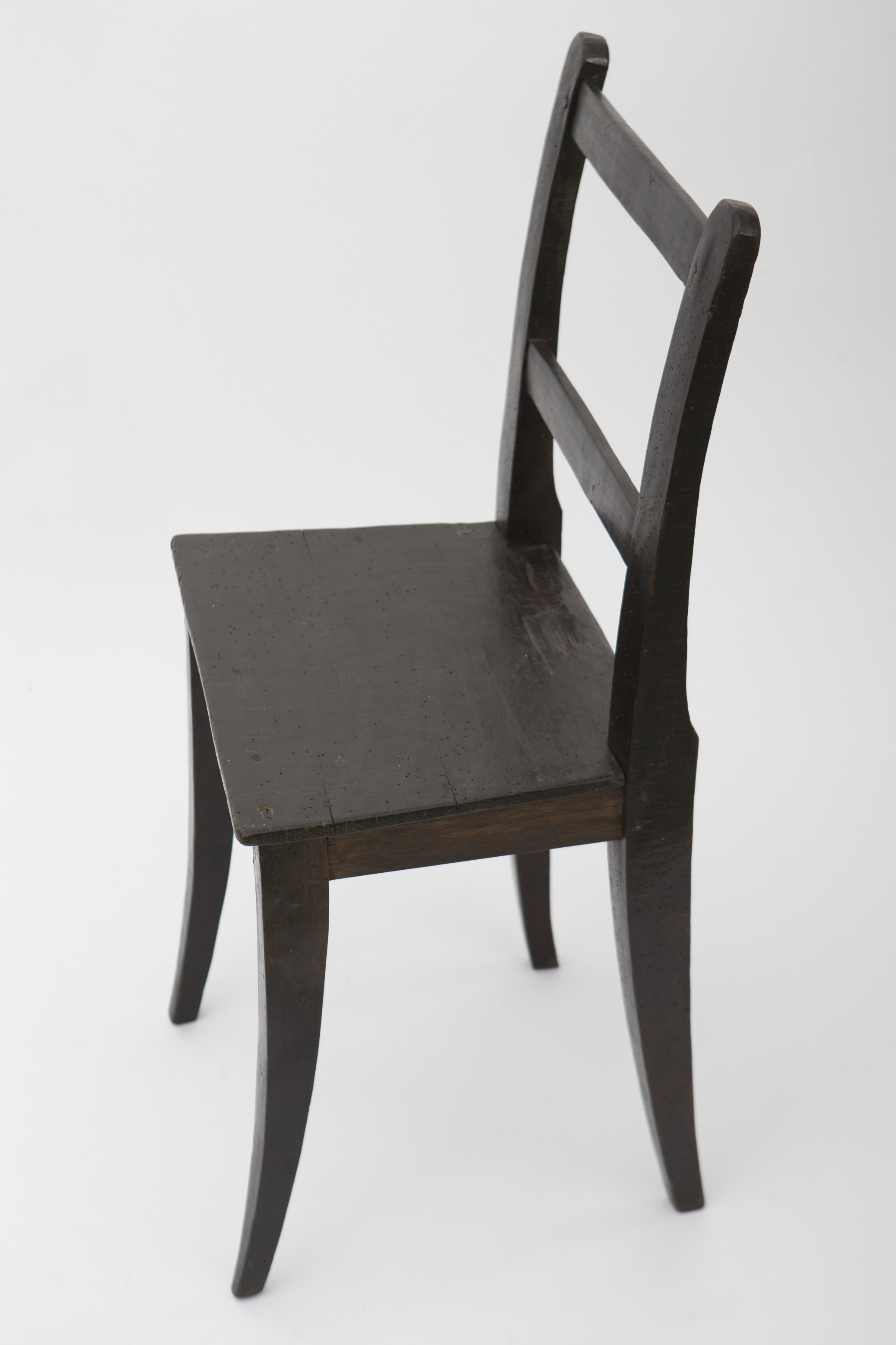 Piesă de mobilier de dimeniuni medii, realizată din lemn de stejar și metal. Scaunul este susținut pe patru picioare, tăiate în patru fețe și ușor evazate. Două dintre picioare, cele din spate, sunt mai înalte decât celelalte două, și formează astfel spătarul. Cele patru picioare și cele patru scânduri orizontale, care le întăresc, susțin blatul de formă trapezoidală. Spătarul prezintă la rândul lui două scânduri orizontale, care întăresc piesa. Nu prezintă decor. Scaunul era folosit pentru mobilarea interiorelor. Prezintă uzură funcțională. Cromatică: maro închis.