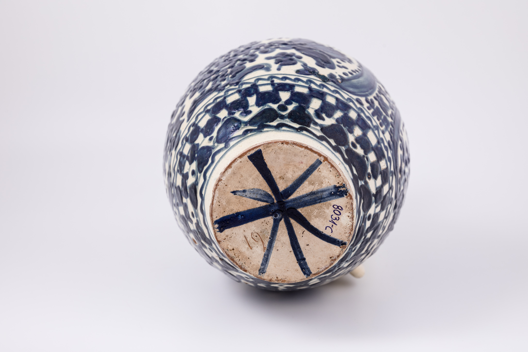 Cană piriformă prevăzută cu o toartă dreaptă și lată, gura rotundă. Suprafața decorativă a vasului este împărțită în trei registre decorative: cel din partea superioară, imediat sub buză, dispus orizontal, cel din mijloc, dispus vertical, iar ultimul, de la bază, orizontal. Primul registru și al treilea prezintă un decor geometric, redat prin linii vălurite, triunghiuri, cercuri și tabla de șah și un motiv fitomorf reprezentat prin brăduți stilizați. Decorul central reprezintă pomul vieții stilizat, separat de semilună și intercalat de motive florale și geometrice așezate vertical: lalele și linii oblice paralele intersectate. „Pomul vieții” este alcătuit din trei lalele mari și vrejuri, intercalate de o multitudine de puncte. Piesa este datată 1833, în partea superioară pomului vieții. De-o parte și de alta a toartei sunt pictate câte două lalele mari. Toarta nu prezintă decor. Cromatica: alb, albastru-cobalt.