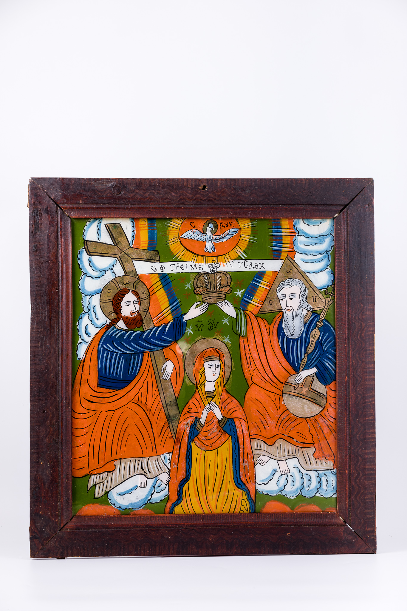 Icoana reprezintă Sfânta Treime și Încoronarea Maicii Domnului. Dumnezeu-Tatăl are globul pământesc pe genunchi. Maica Domnului este ridicată în timpul de rugăciune și ascultare, smerenie și primire de bunăvoie. Dumnezeu-Tatăl, Dumnezeu-Fiul și Maica Domnului sunt înveșmântați în roșu vermillon, bej, ocru, alb și albastru cobalt. În registrul îndepărtat superior este văzduhul verde văratic, plin de Duhul Sfânt, Dumnezeu-Fiul ține pe brațul stâng Crucea, iar Maica Domnului are mâinile împreunate în cruce pe piept. Dumnezeu-Tatăl și Dumnezeu-Fiul așează împreună coroana de împărăteasă a Cerurilor pe capul Fecioarei Maria. Deasupra este Sfântul Duh, sub forma porumbelului alb pogorât din Cerurile deschise, dintr-o mandorlă de nouri albi rotunzi și un soare roșu-orange pe un mănunchi de raze luminoase. Razele luminoase formează un curcubeu, în cele trei culori ale steagului românesc: roșu, galben și albastru. Inscripția din româno-chirilică se traduce Sfânta Treime Tatăl Sf Duh MP Maica Domnului. Cromatica este armonioasă și luminoasă: roșu vermillon, galben chihlimbar, verde văratic, albastru cobalt, bej, alb, negru. Icoana este din Țara Oltului.
