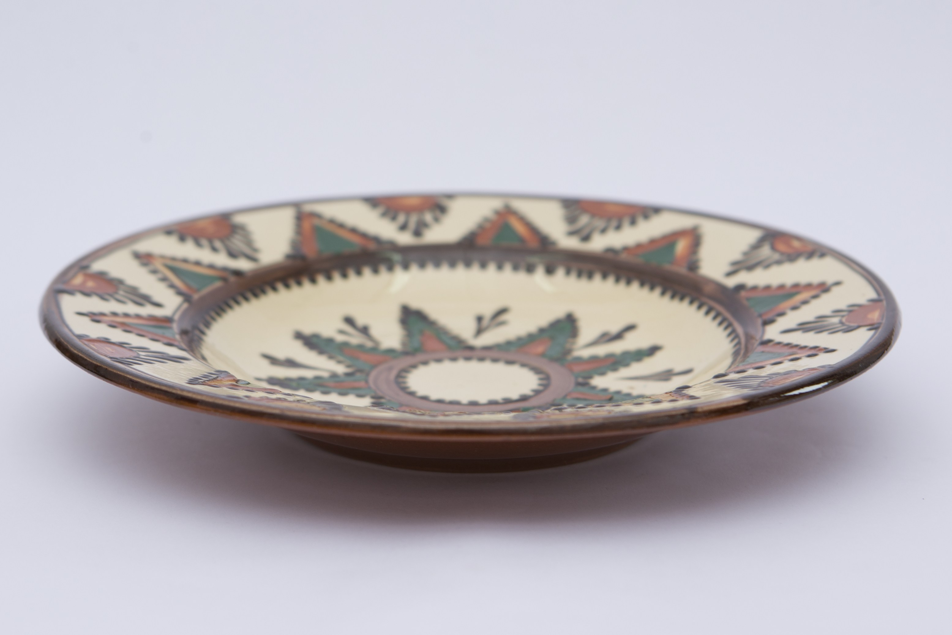 Disc plat cu margini curbate; buza aproape orizontală; decor: linie la margine; fund: stea cu opt colțuri; pe buză: colț de stea și puncte în relief și semicercuri de picături scurse; interior angobat și smălțuit; fund nesmălțuit. Cromatică: fond: alb; motive: maro; verde; cărămiziu.