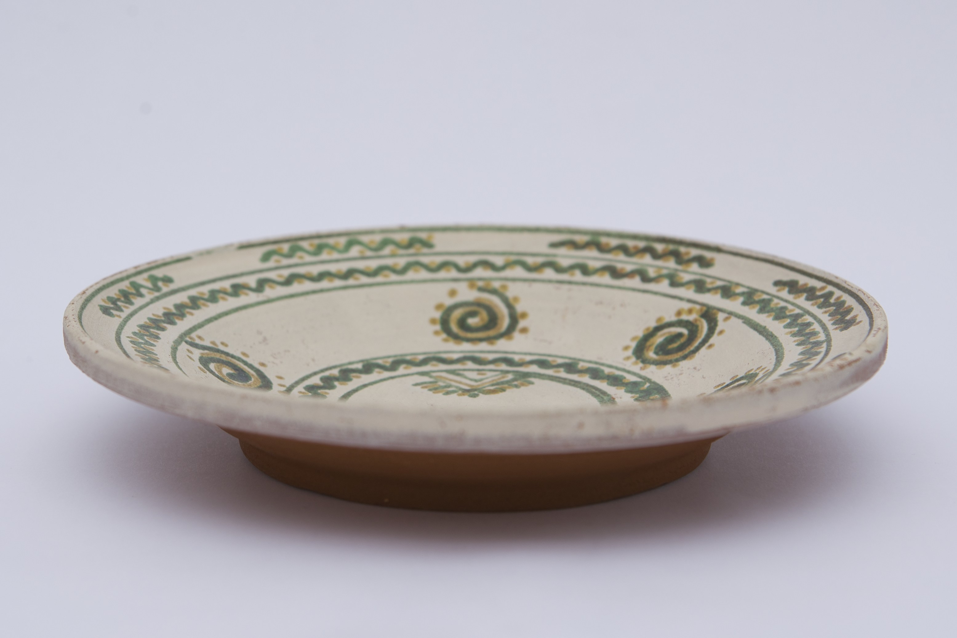 Vas ceramic de formă discoidală pe bază puțin înălțată. Fața farfuriei a fost introdusă în angobă albă, decorația a fost făcută cu pensula. Pe fundul vasului sunt două cercuri concentrice: în primul sunt doi brăduți, iar în al doilea valul punctat. Pe pereți sunt șase spirale punctate. Marginea vasului a fost împărțită în două registre, primul cu val punctat, în al doilea sunt șapte valuri întrerupte. La posterior, pe fund, semătura ”D Șchiopu ''. Pentru atârnare baza este perforată. Cromatică: fond: alb; motive; verde; galben.