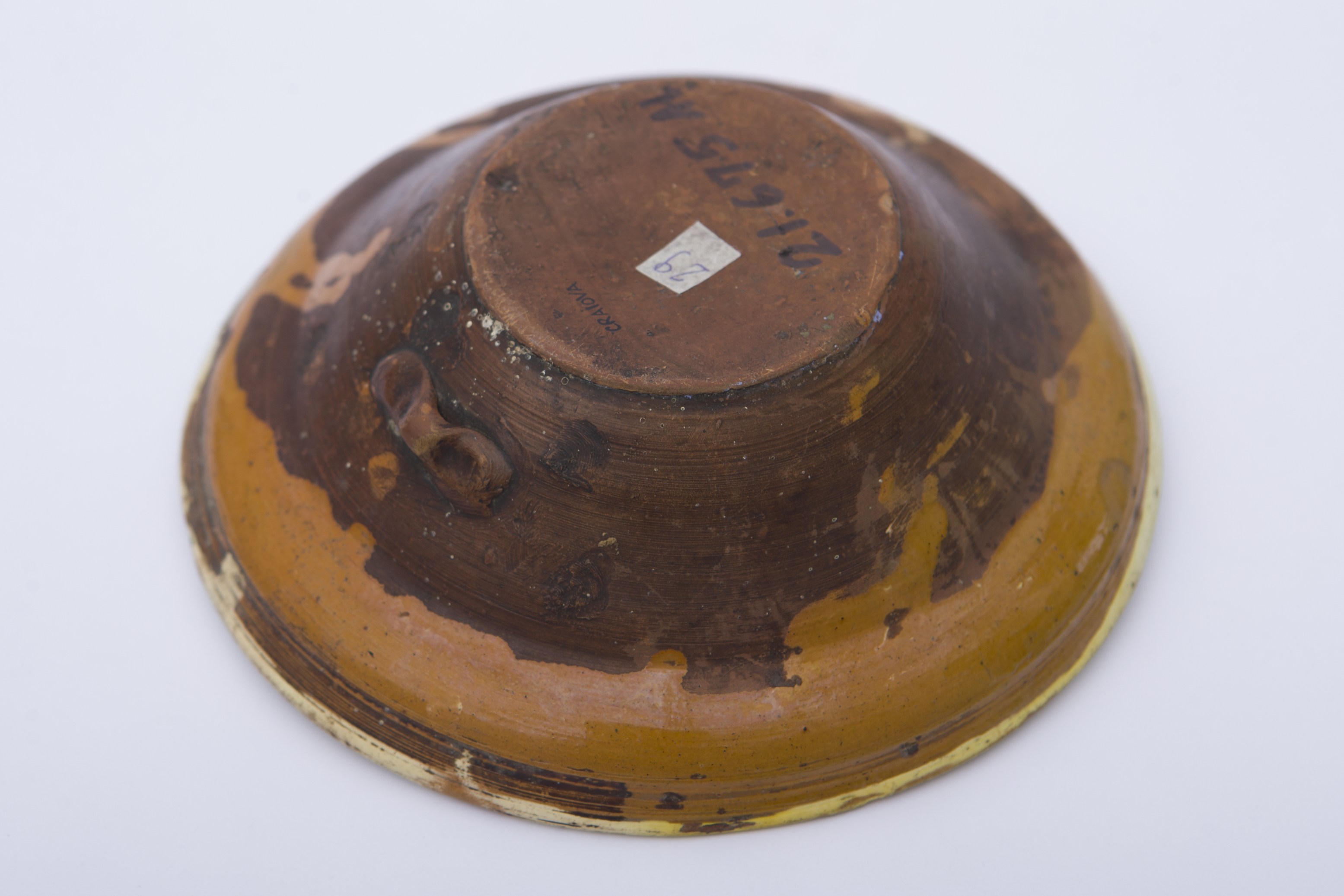 Vas ceramic smălțuit de formă tronconică. Pe fundul vasului dispusă o floare albastră cu frunze verzi. Același motive dispuse circular pe marginea vasului. Cromatică: fond: crem; motive: verde; albastru.