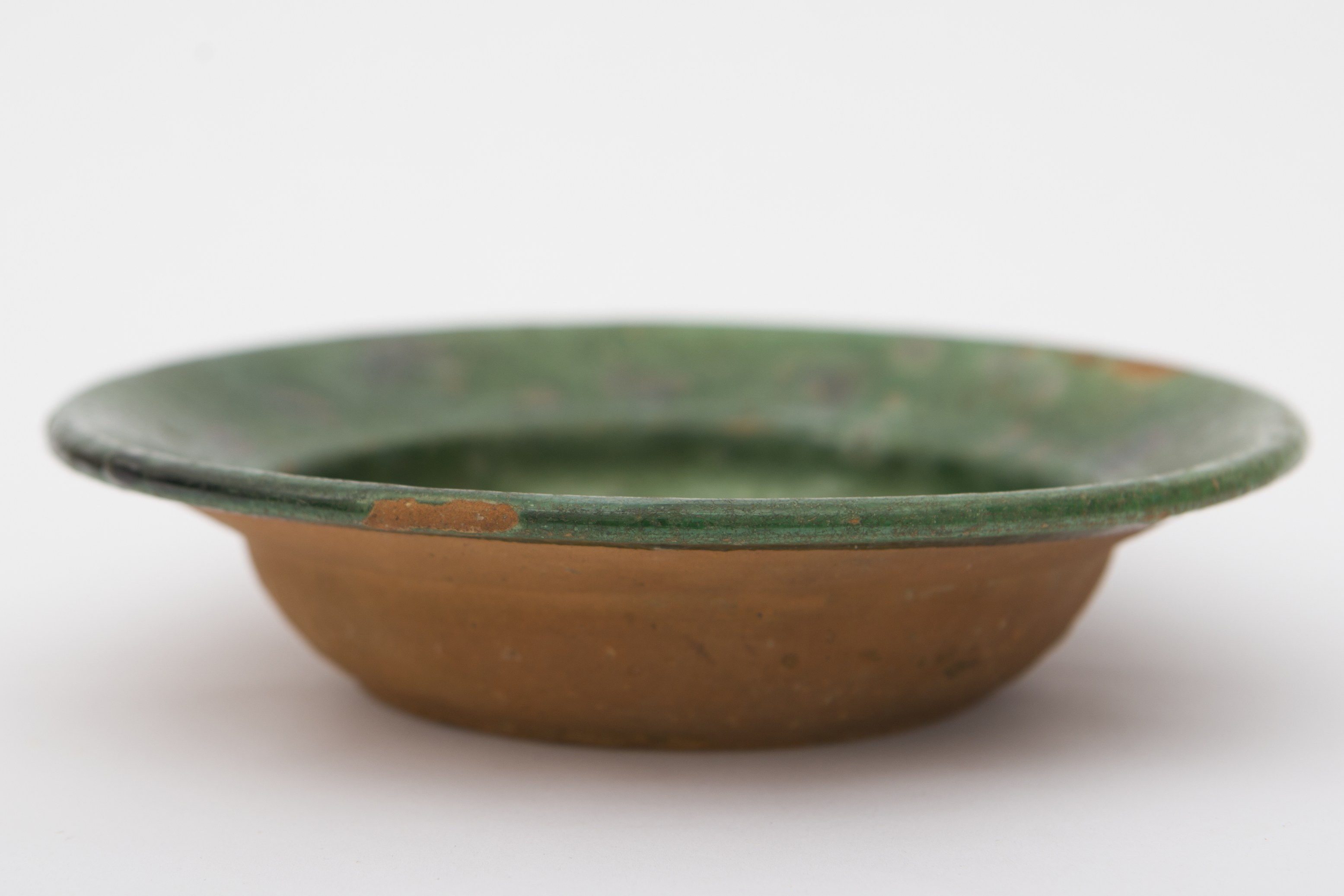 Vas ceramic smălțuit în interior, de formă tronconică, cu baza plată, pereții puțin ridicați și marginile evazate. Recipientul prezintă un strat gros de angobă verde pe toată suprafața interioară. Pe alocuri pete de culoare ușor diferită. Fundul și marginile vasului prezintă decor geometrizant incizat: linii succesive, dispuse circular. Pe spate prezintă o ”tortiță” de mici dimensiuni pentru suspendare pe perete. Blidul era utilizat în gospodărie pentru servirea hranei. Prezintă uzură funcțională. Cromatică: cărămiziu (exterior); verde (interior).