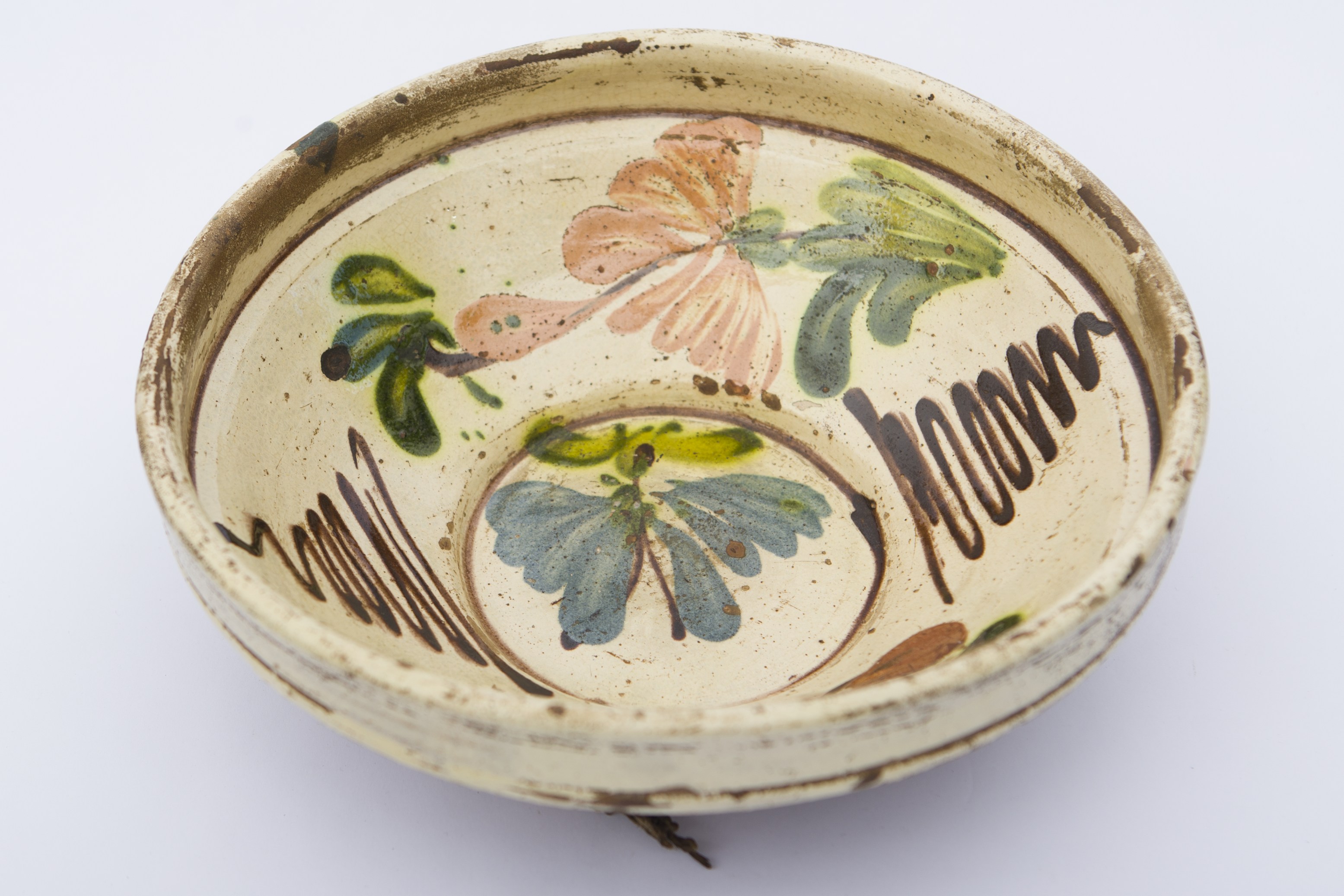 Piesă ceramică, smălțuită în interior, de formă tronconică cu baza plată, pereții înalți și buza profilată. Peste fondul alb au fost realizate prin pictare decorații, ilustrând trei flori, dintre care una cu petale albastre aflată pe fundul vasului, încercuită de o linie maro. Alte două flori, de culoare maro roșcat sunt dispuse pe pereții interiori ai vasului în alternanță cu frunze verzi separate de două registre de linii vălurite, de culoare maro închis. Pe spate prezintă două orificiii pentru suspendare. Blidul era folosit pentru servirea hranei sau ornamentarea interioarelor. Prezintă uzură funcțională. Cromatică: fond: cărămiziu (exterior); alb (interior); motive: verde; maro închis; maro roșcat; albastru.