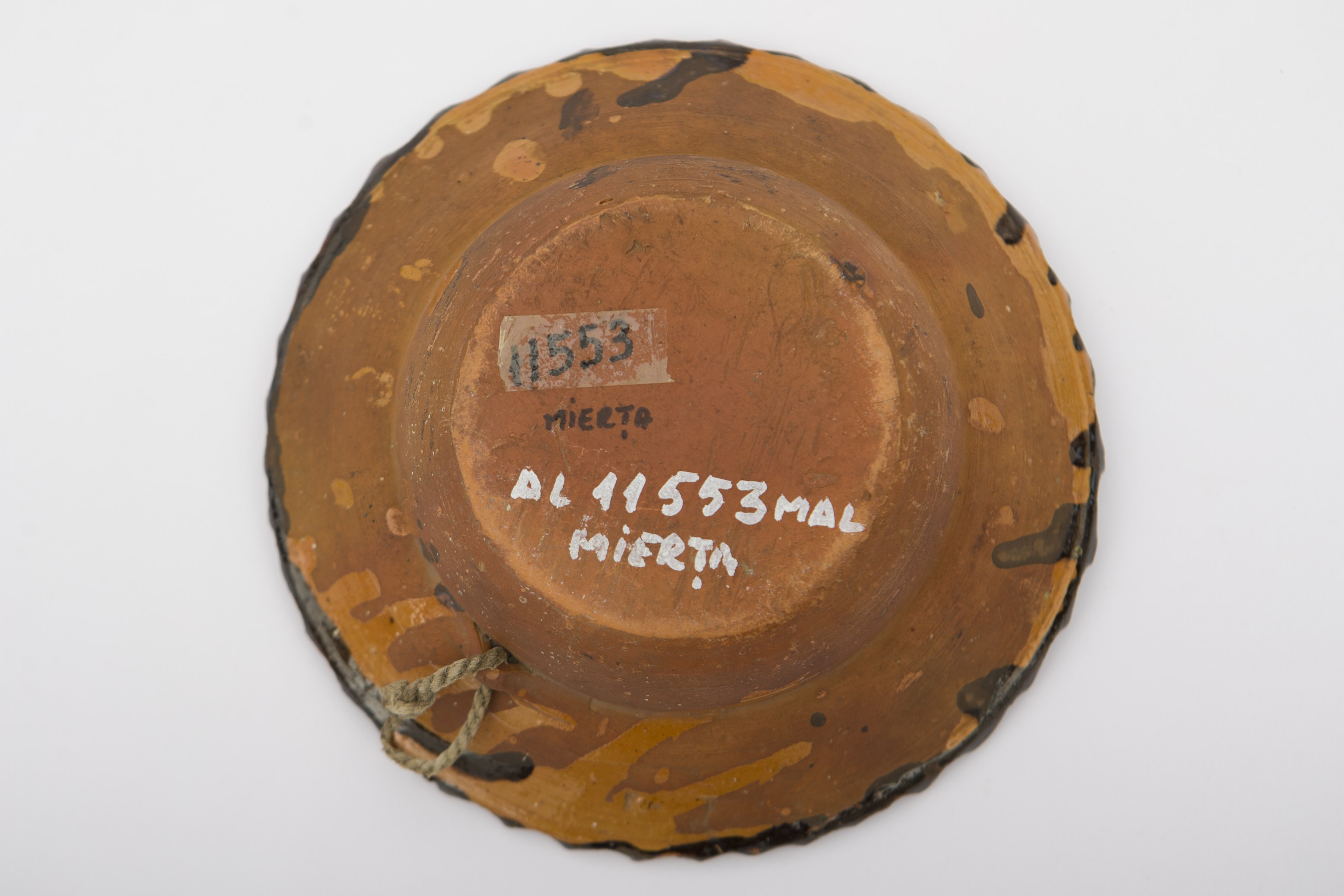 Piesă ceramică smălțuită în interior, de formă tronconică, cu baza plată, pereții puțin ridicați și buza larg evazată. Peste fondul negru a fost realizat decorul fitomorf stilizat, reprezentând cinci flori cu câte patru petale albe și câte un punct maro, măginit de puncte albastre. Una dintre flori se află pe fundul vasului. Celelalte patru flori sunt dispuse pe marginile vasului și sunt unite de trei șiruri punctate dispuse circular. Șirul din mijloc, de culoare verde este mărginit de celelalte două albe. Bordura vasului este zimțată. Pe spate prezintă o ”tortiță” de mici dimensiuni pentru suspendare pe perete. Vasul era folosit în gospodărie pentru decorarea interioarelor. Prezintă uzură funcțională. Cromatică: fond: cărămiziu (exterior); negru (interior); motive: alb; verde; albastru; maro roșcat.