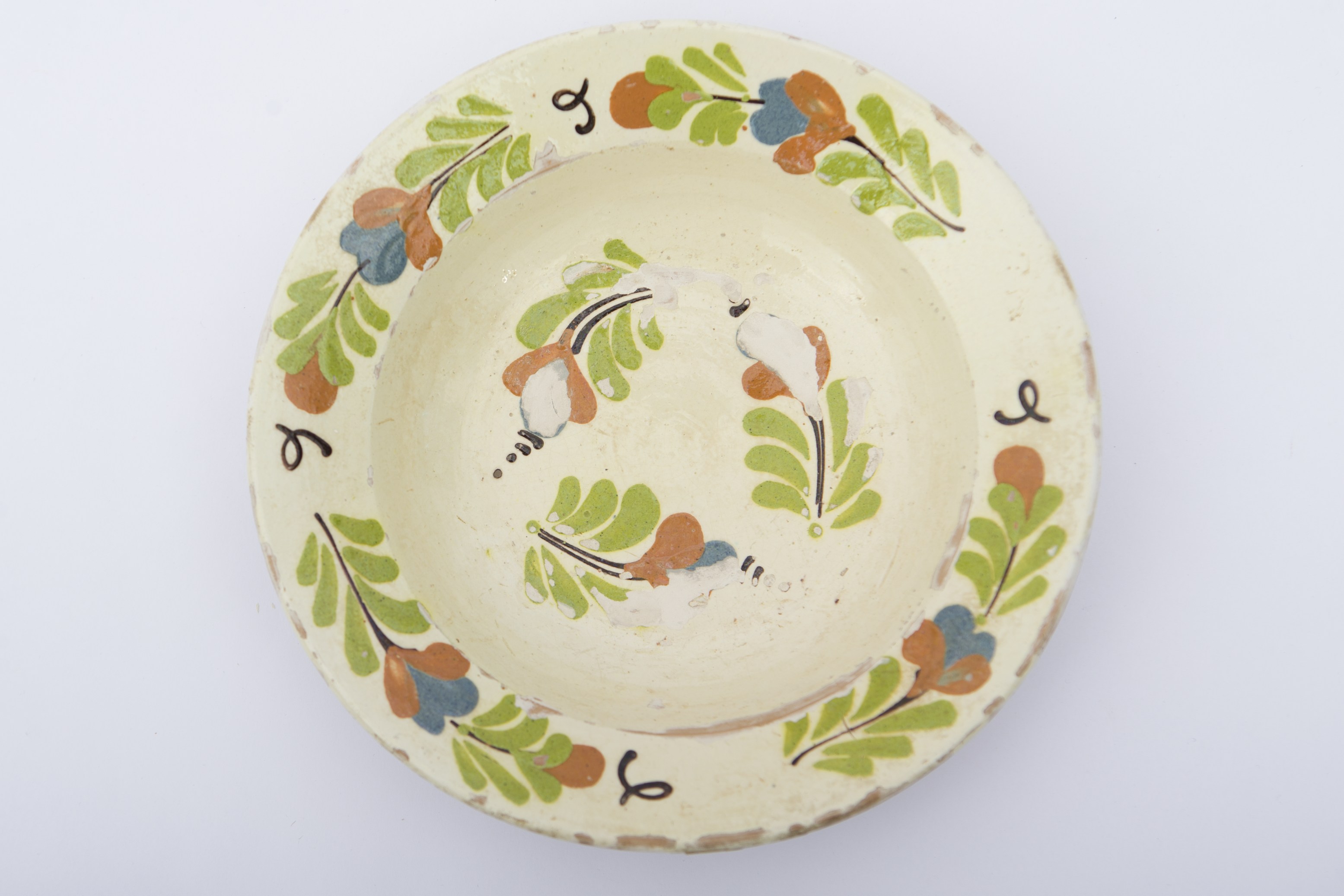 Vas ceramic smălțuit în interior, de formă tronconică, cu baza plată, pereții ușor ridicați și buza evazată. Pe fond alb decorații fitomorfe realizate prin pictare cu pensula, ilustrând flori cu petale maro și albastre, tulpini albastre și frunze verzi. Trei flori cu petale albastre și maro, sunt dispuse circular pe fundul vasului. Celelalte sunt dispuse concentric în patru registre pe marginile vasului, având în continuare câte un boboc de floare maro cu frunze. Registrele sunt despărțite de câte patru linii ondulate. Pe spate prezintă o ”tortiță” de mici dimensiuni pentru suspendare pe perete. Piesa era folosită în gospodărie pentru servirea hranei, dar și pentru ornamentarea interioarelor. Prezintă uzură funcțională. Cromatică: fond: cărămiziu (exterior); alb (interior); motive: verde; albastru; maro roșcat.