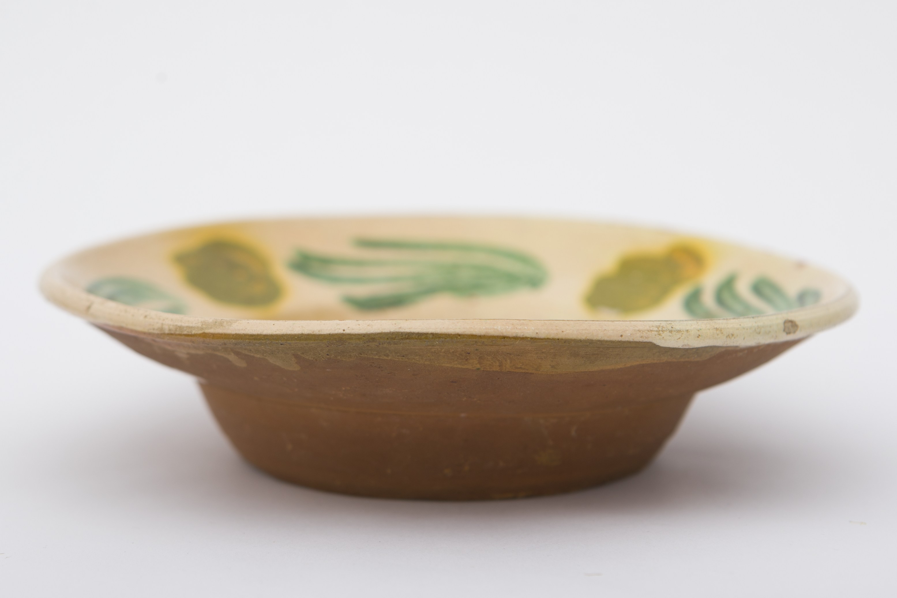 Vas ceramic smălțuit în interior, de formă tronconică, cu baza plată, pereții ușor ridicați și buza evazată. Pe fond crem, au fost realizate prin pictare decorații ilustrând cinci flori în culoarea galben închis cu frunze lungi în culoarea verde. Una dintre flori dispusă pe fundul vasului având cinci frunze. Celelalte patru sunt dispuse circular pe marginile vasului având câte cinci frunze fiecare. Pe spate prezintă o ”tortiță” de mici dimensiuni pentru suspendare pe perete. Blidul era folosit în gospodărie pentru servirea hranei sau ornamentarea interioarelor. Prezintă uzură funcțională. Cromatică: fond: cărămiziu (exterior); crem (interior); motive: verde; galben.