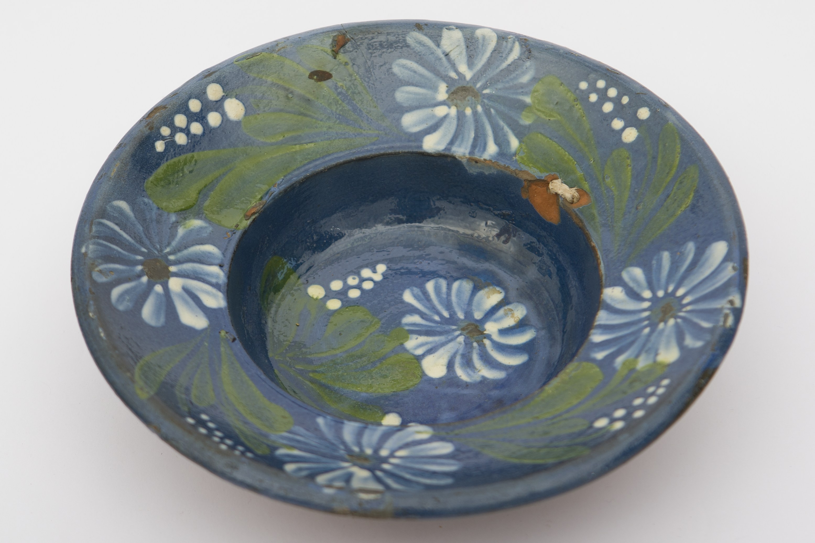 Vas ceramic smălțuit în interior, de formă tronconică cu baza plată, marginile puțin ridicate și buza profilată. Pe fond albastru, au fost pictate decorații fitomorfe, ilustrând cinci flori cu petale albe și conturate cu alb-bleu, cu câte un punct verde închis în mijloc, frunze verzi și linii punctate, ce se subțiază spre vârf. Una dintre flori încadrată de două linii puctate ce se subțiază spre vârf, se află pe fundul vasului. Celelalte flori, în alternanță cu frunze și linii punctate sunt dispuse pe marginile vasului. Pe spate prezintă două orificii pentru suspendare. Blidul era folosit în gospodărie pentru decorarea interioarelor. Prezintă uzură funcțională. Cromatică: fond: cărămiziu (exterior); albastru (interioară); motive: alb; verde.