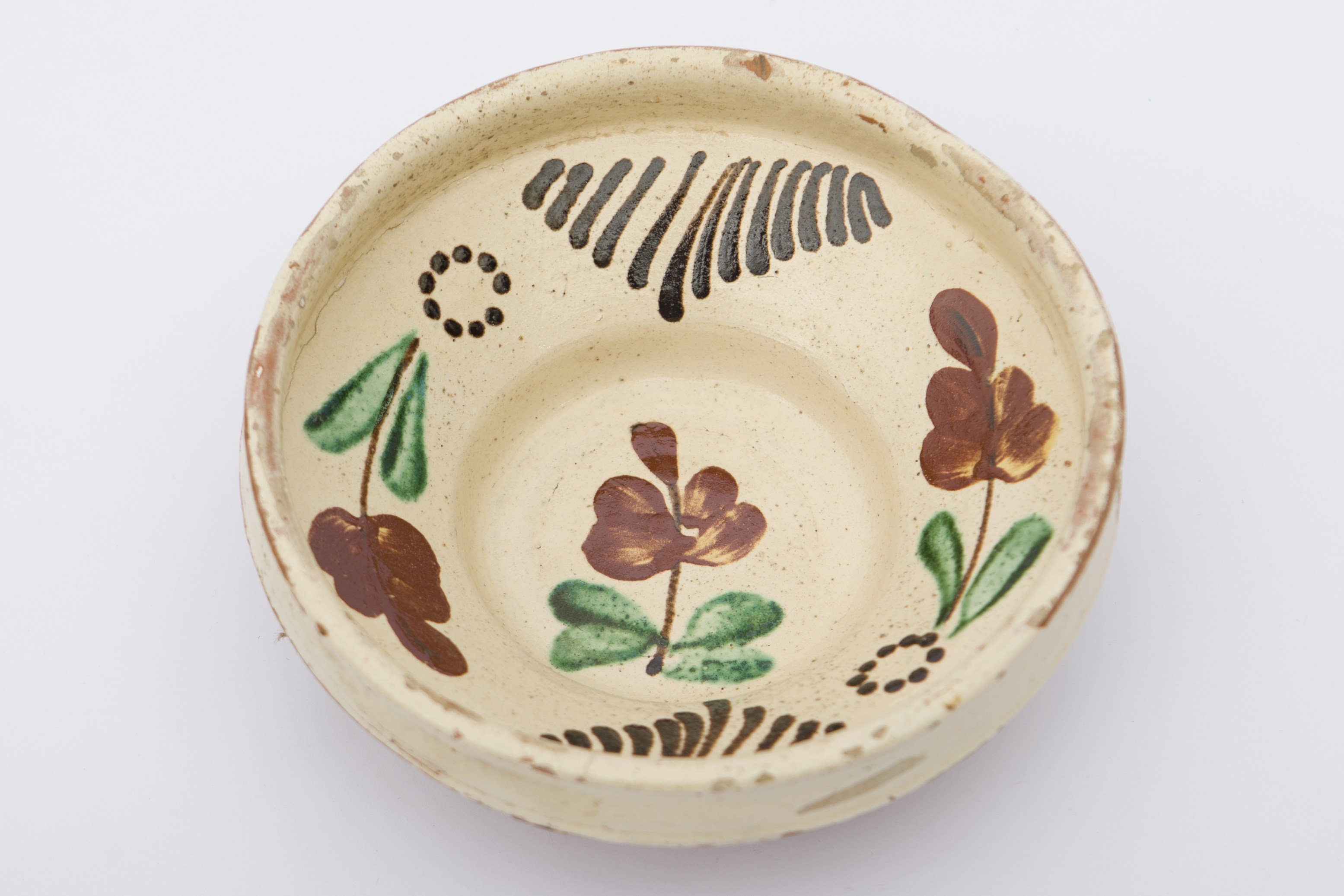 Recipient ceramic smălțuit în interior, de formă tronconică, cu baza plată, marginile puțin ridicate și profilată. Pe fond alb a fost realizat decor fitomorf, pictat cu pensula: trei flori cu petale maro roșcat, tulpină maro închis și frunze verzi. Una dintre flori cu patru frunze se află pe fundul vasului. Celelalte două, în antiteză una față de cealaltă, având câte două frunze, fiecare dispuse concentric pe peretele interior, având la bază câte un cerc format din puncte negre. Există și două grupe de linii verticale negre dispuse pe peretele interior. Pe spate prezintă o ”tortiță” de mici dimensiuni pentru suspendare pe perete. Blidul era folosit în gospodărie pentru servirea hranei sau decorarea interioarelor. Prezintă uzură funcțională. Cromatică: fond: cărămiziu (exterior); alb (interior); motive: maro închis; maro roșcat; verde.